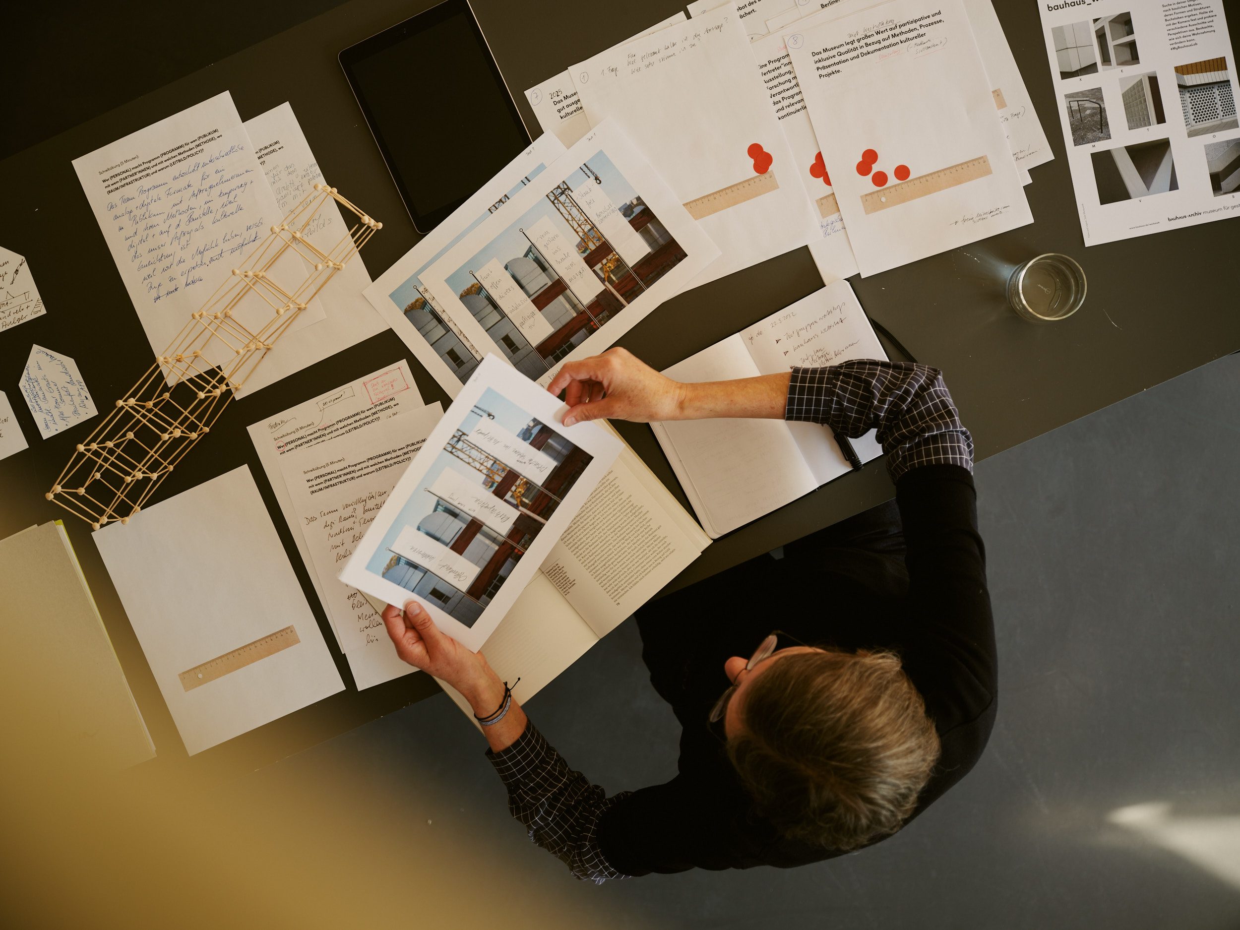 Foto einer Person, die an einem Tisch arbeitet, umgeben von Dokumenten und Entwürfen. Sie betrachtet Workshopergebnisse zu Nachbarschaftsstudien.