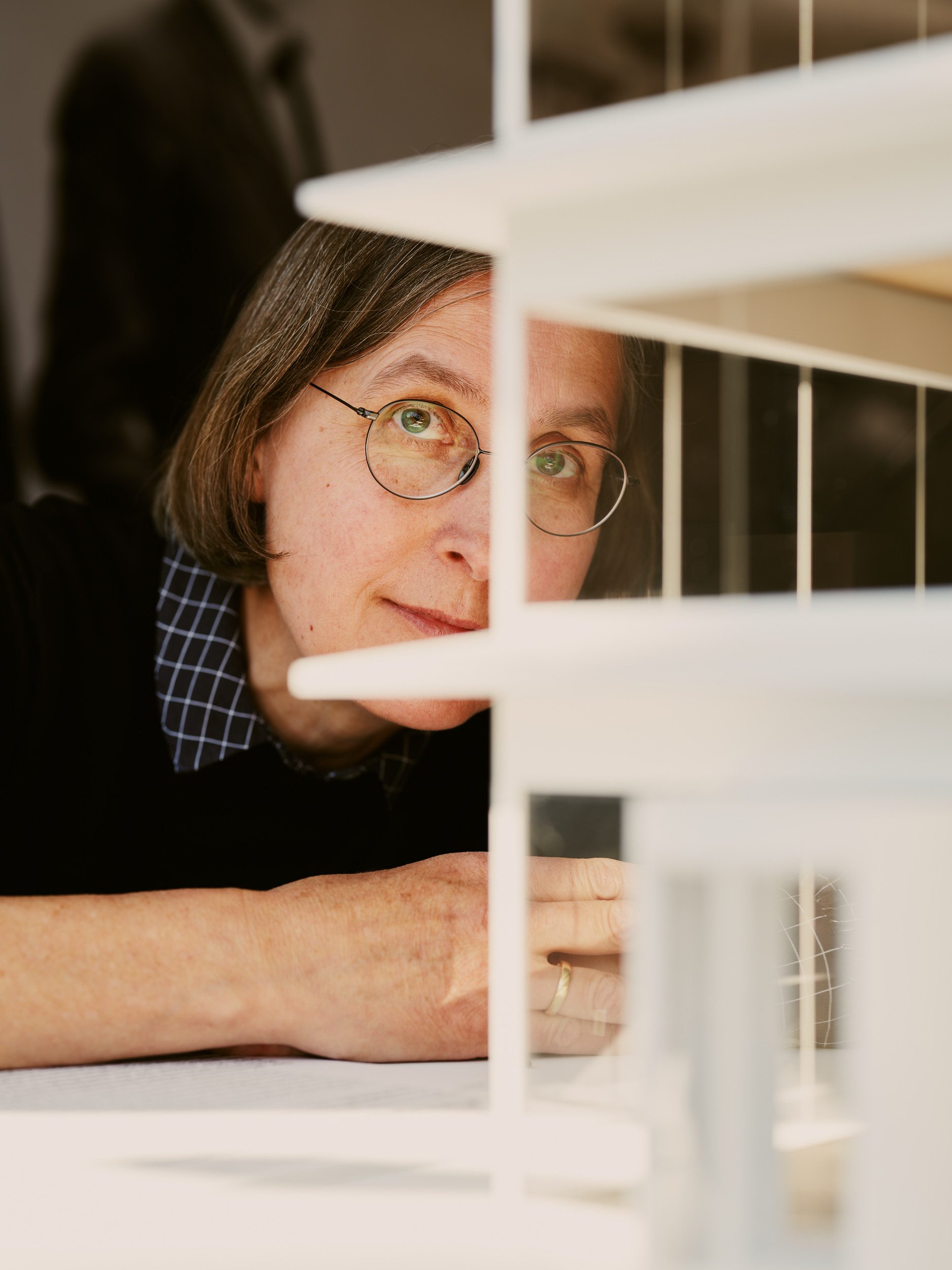 Foto einer Frau mit Brille, die aufmerksam das weiße Architekturmodell des Neubaus betrachtet.