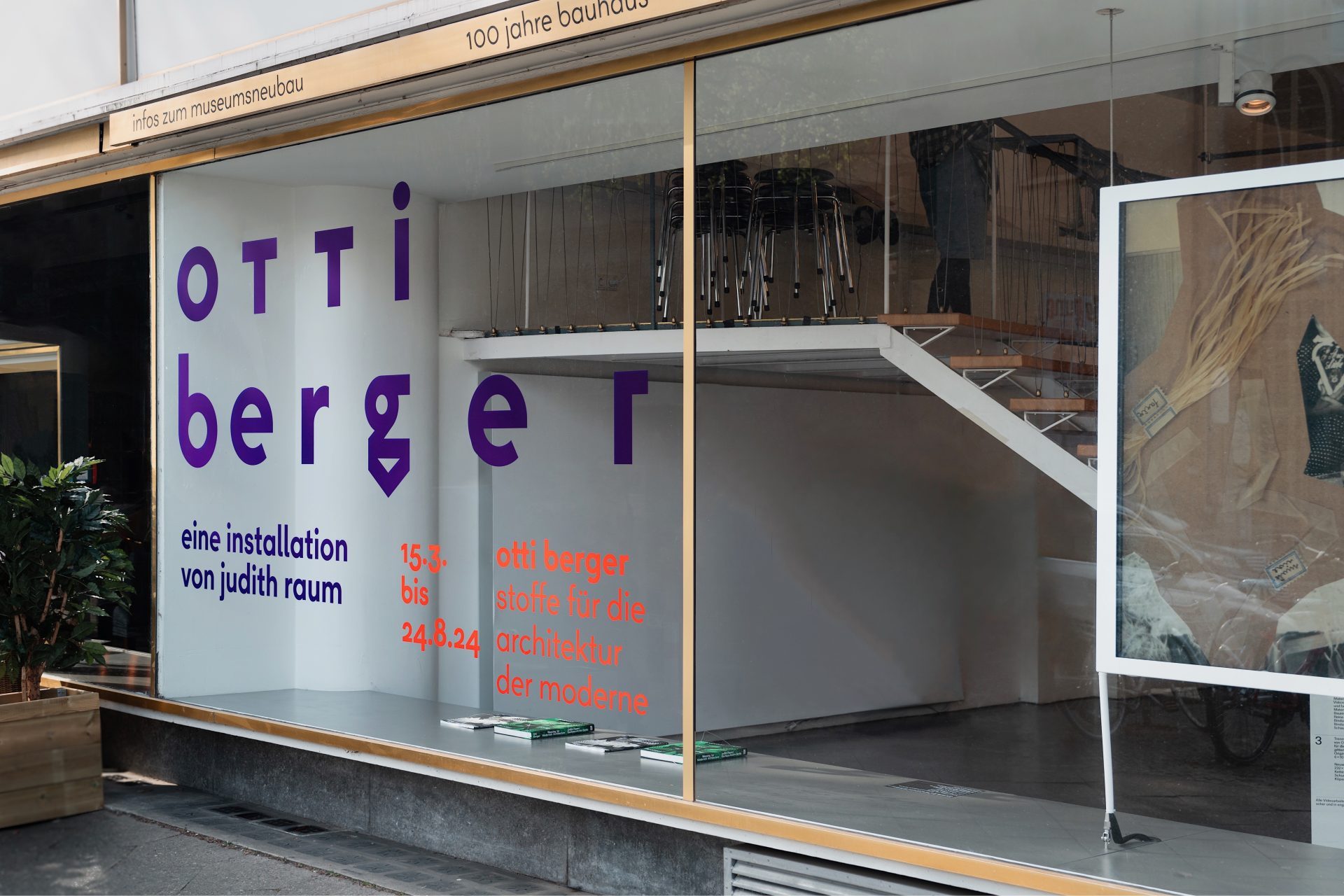 Foto des Schaufensters im Temporary Bauhaus-Archiv mit dem Titel der Ausstellung in lilaner und roter Schrift. Blick in den minimalistischen Innenraum.