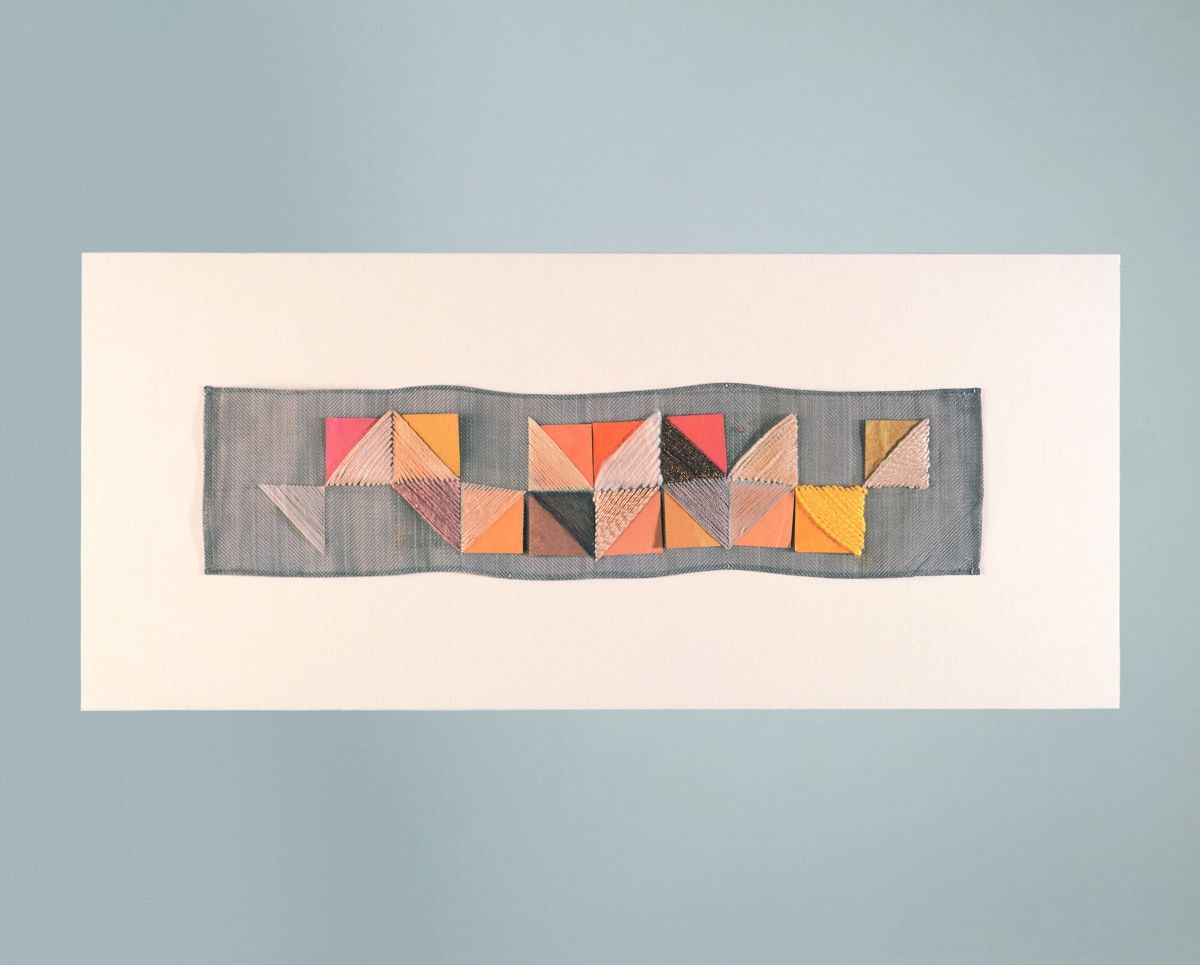 Foto einer abstrakten bunten Collage aus geometrischen Formen in unterschiedlichen Farben aus Stoff, weiß umrandet und vor grauem Hintergrund.