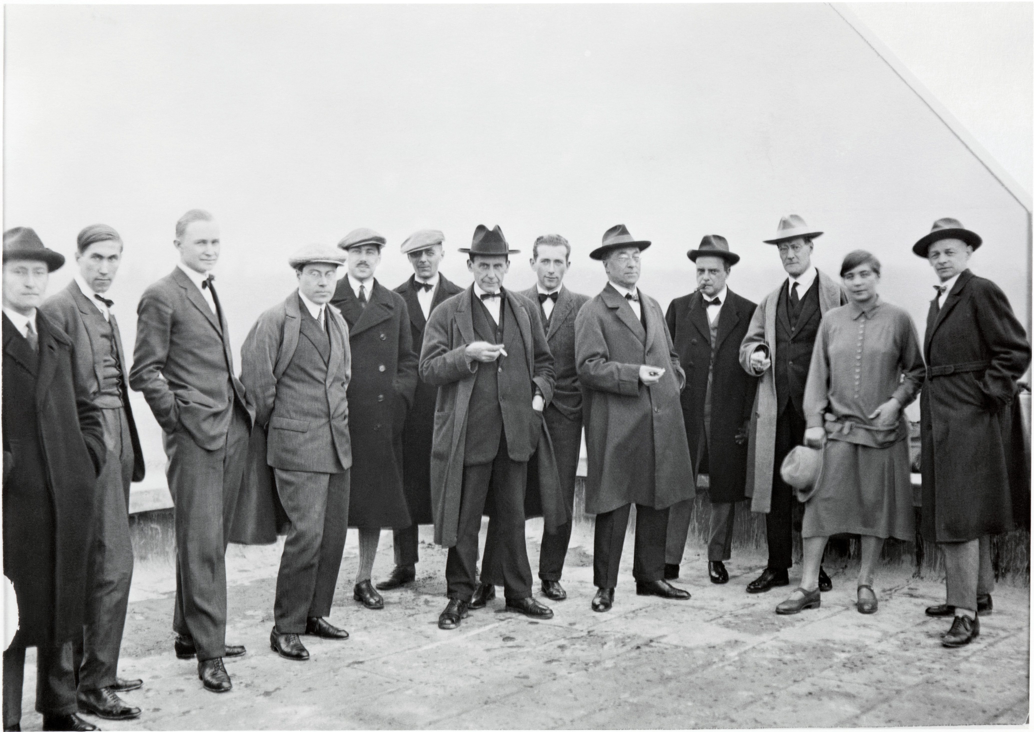 A group of men and one woman in early 20th-century attire, posing together outdoors.