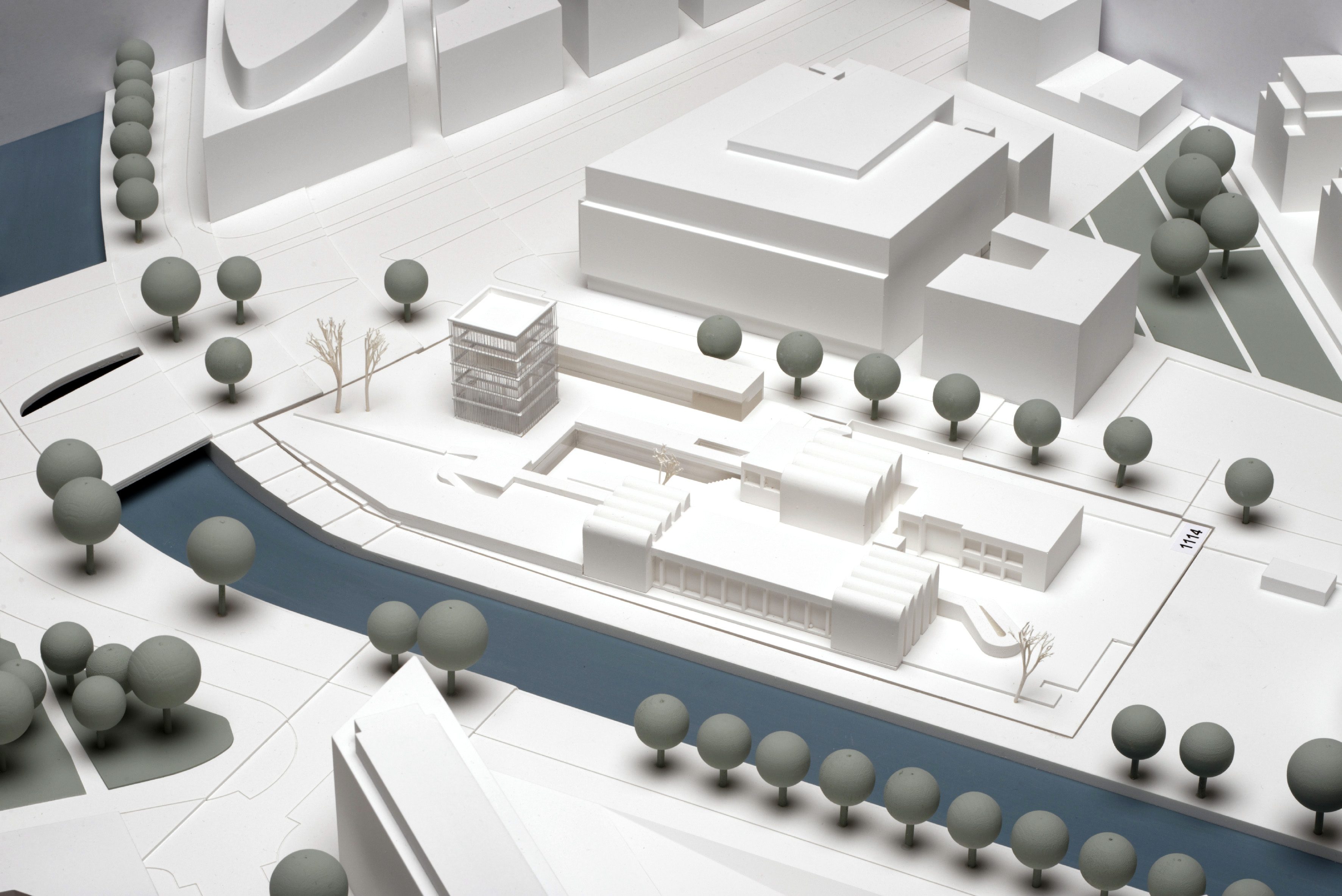 Architekturmodell mit weißen Gebäuden, Bäumen und einem Fluss in minimalistischer Gestaltung.