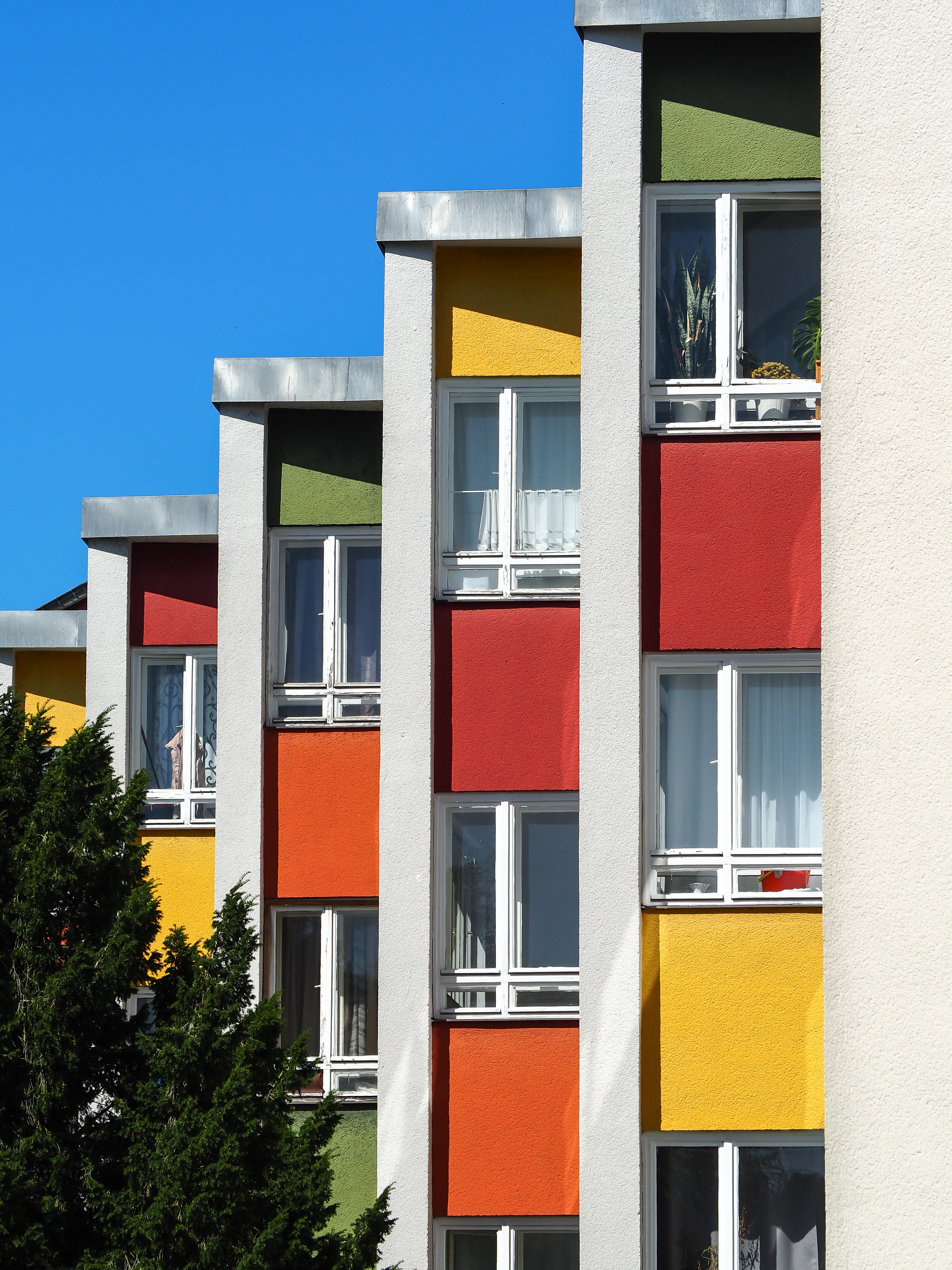 Fassade eines modernen Gebäudes mit bunten Farben und großen Fenstern unter klarem blauen Himmel.