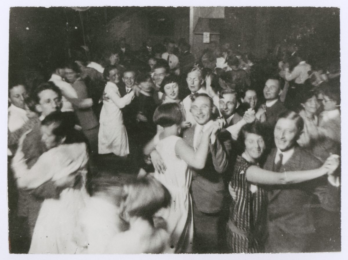 Black-and-white photo of a joyful dance event with many people in elegant attire.