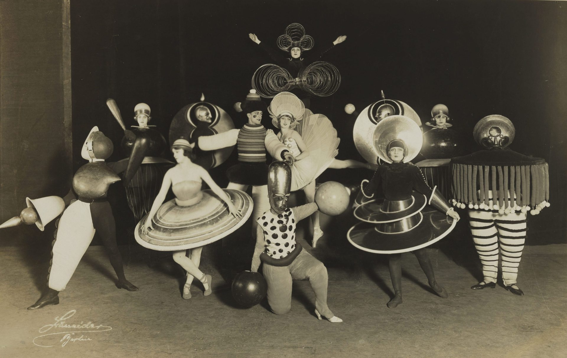 Artistic group in imaginative costumes with geometric shapes and eye-catching accessories on a stage.