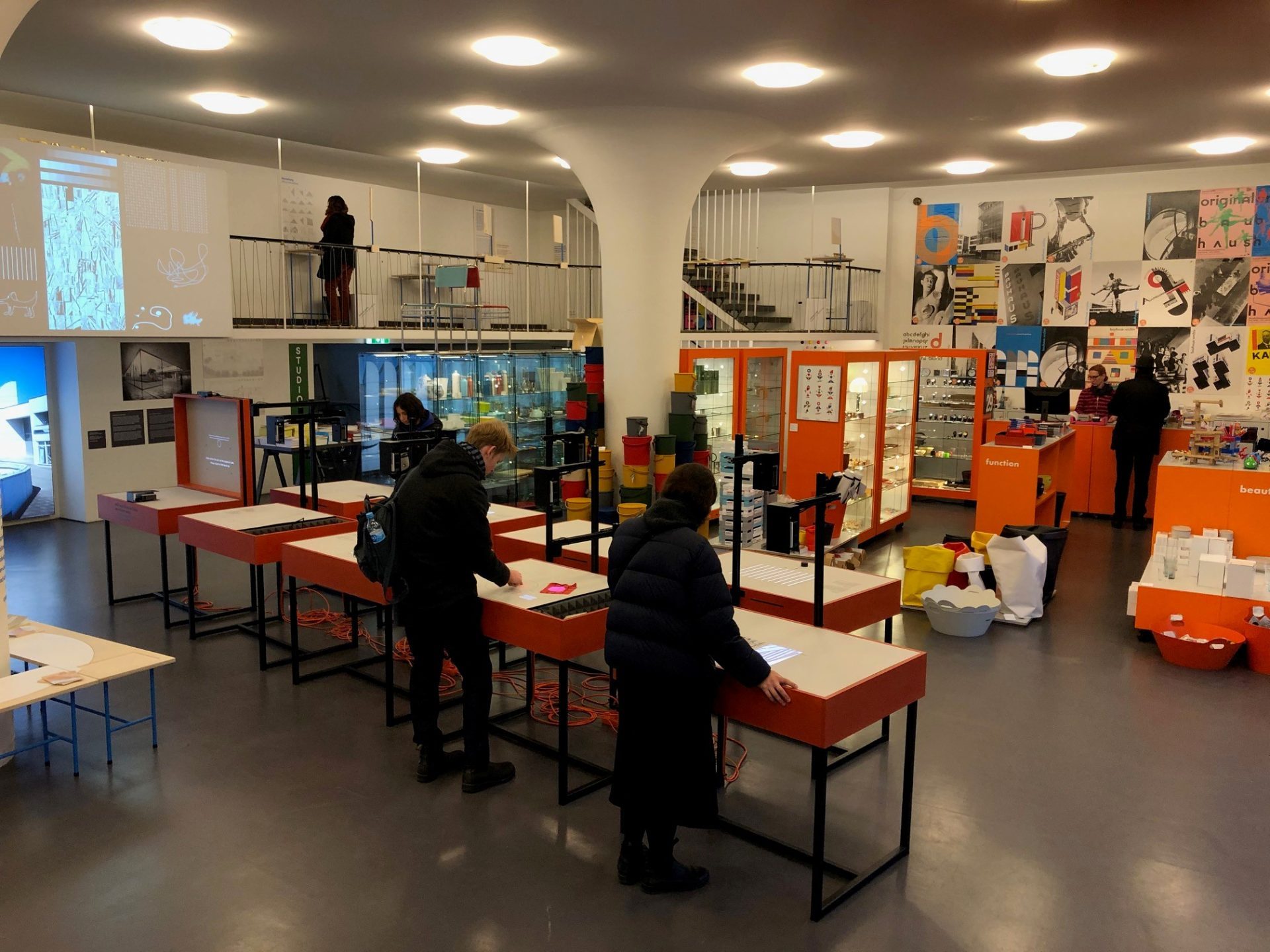 In einem modernen Ausstellungsraum erkunden Besucher interaktive Tische und Regale mit bunten Objekten und Kunstwerken.