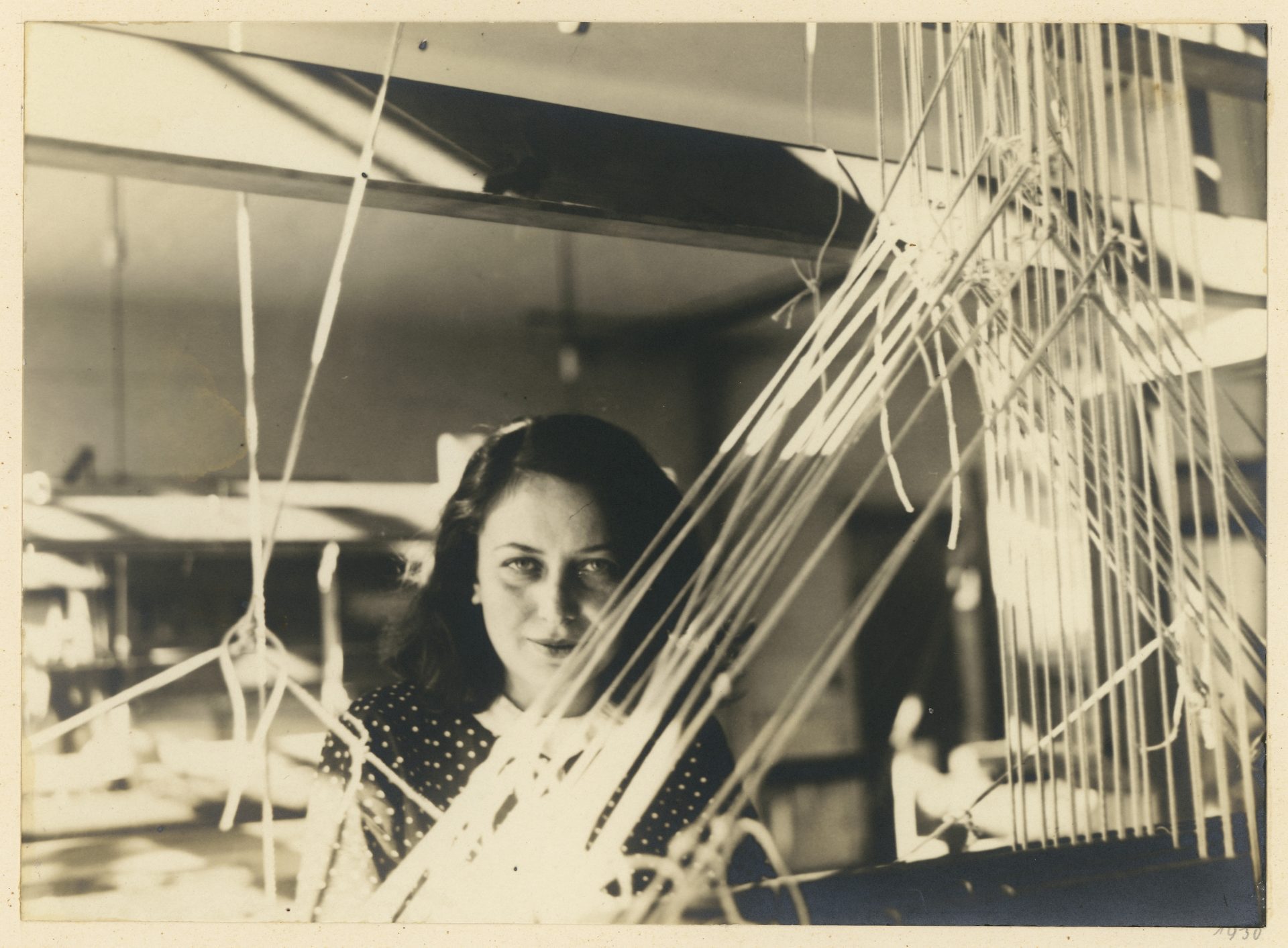 A woman with dark hair and a polka-dot dress looks through tangled threads in a studio or workshop.
