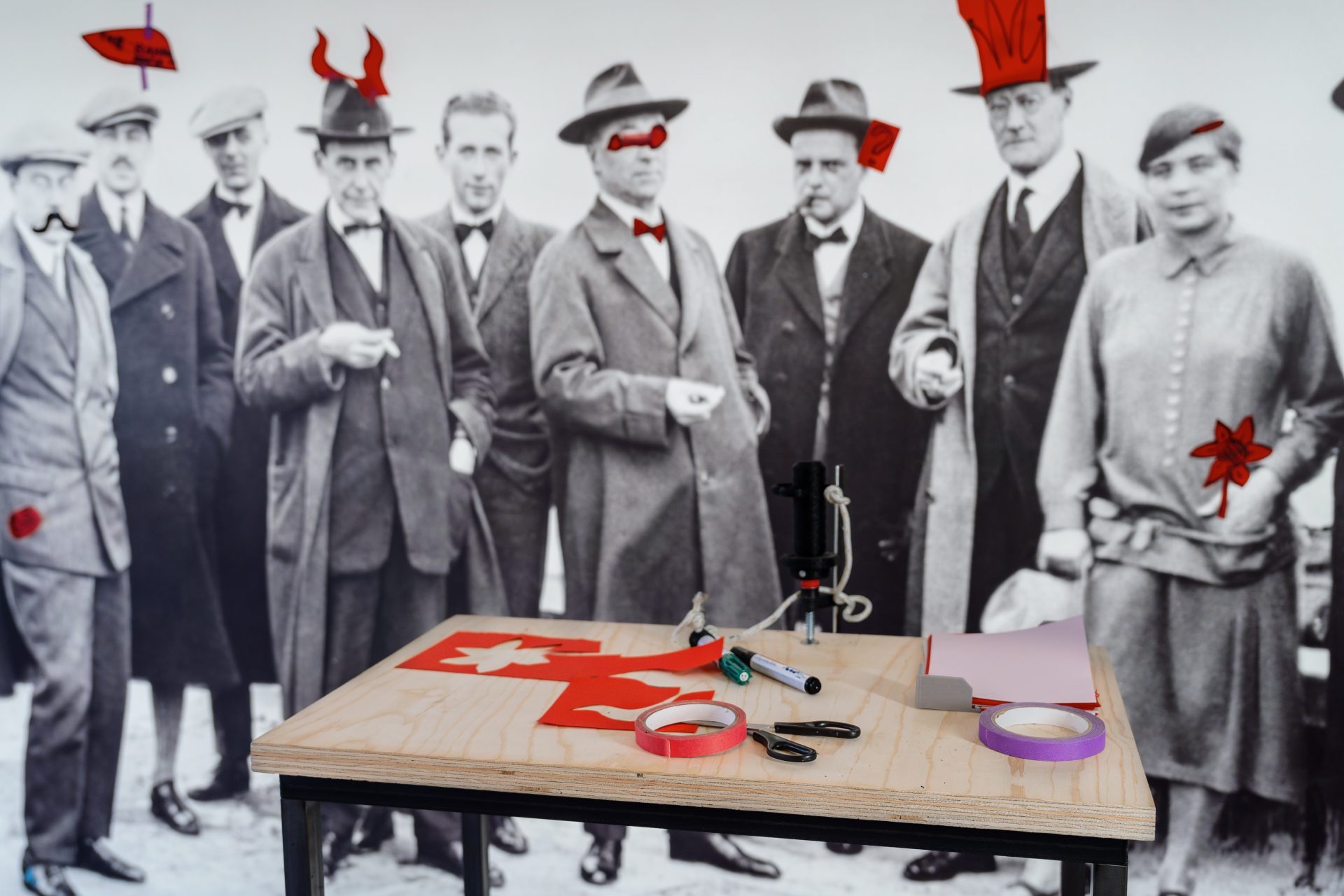 Schwarz-weiß-Foto einer Gruppe von Männern und Frauen, neben einem Tisch mit Werkzeugen und Bastelmaterialien.