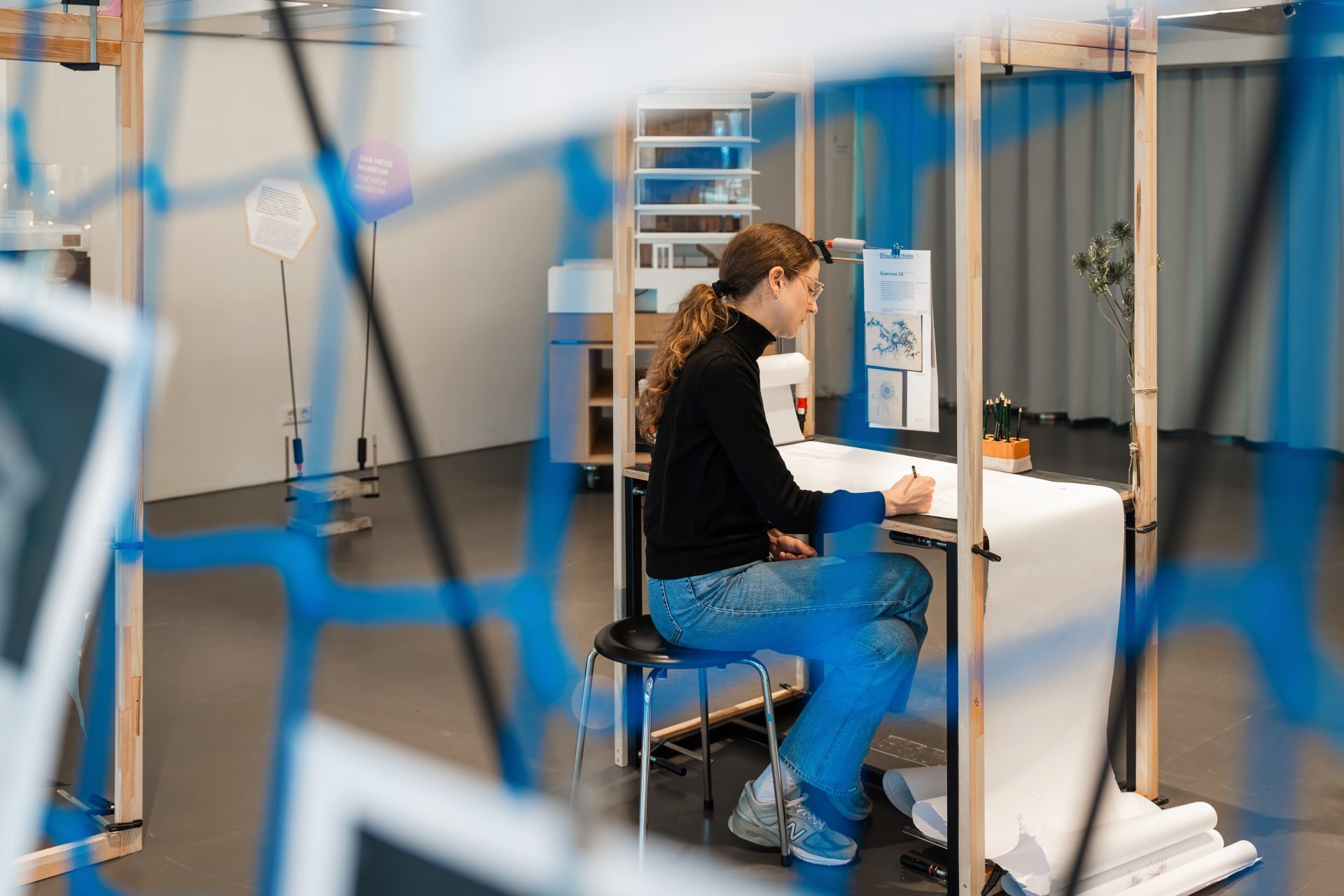 Eine Frau sitzt an einem Tisch und arbeitet in einem modernen, hellen Raum, umgeben von einer blauen Netzstruktur.