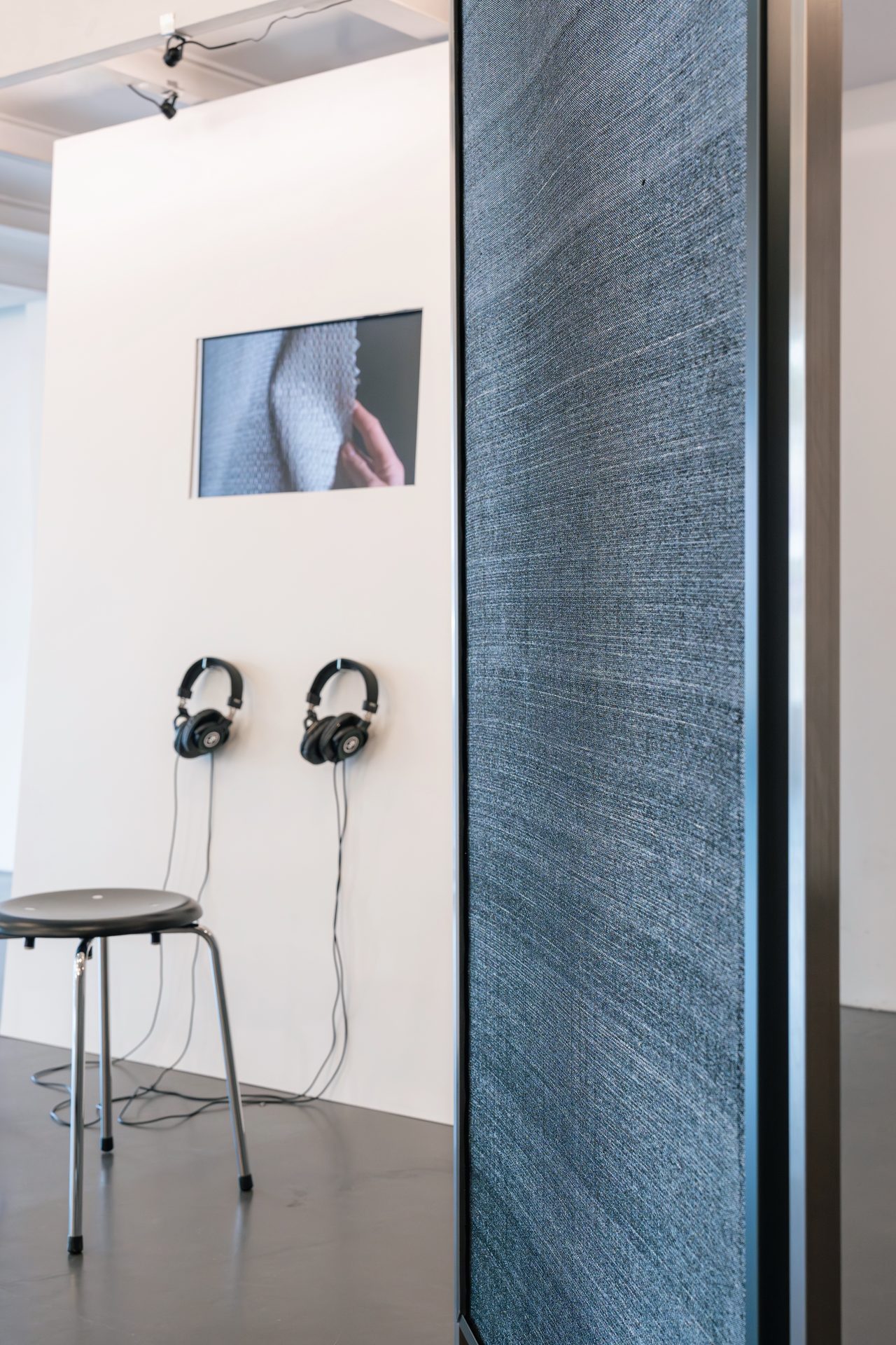 Kunstinstallation mit Kopfhörern, einem Stuhl und einem Wandbildschirm, der eine Nahaufnahme zeigt.