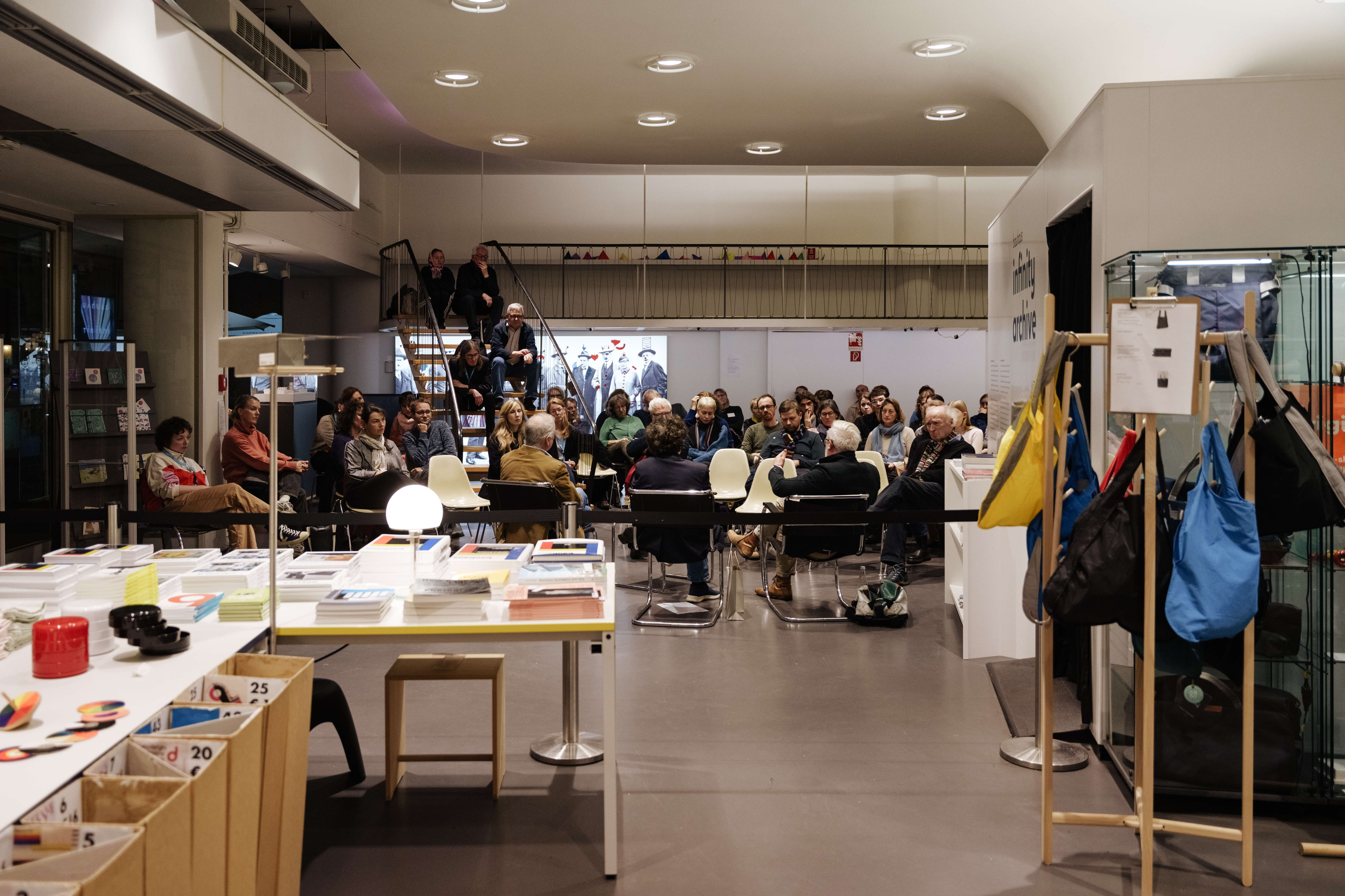 Besucher bei einer Veranstaltung in einem modernen Raum mit Tischen, Stühlen und Ausstellungsflächen.