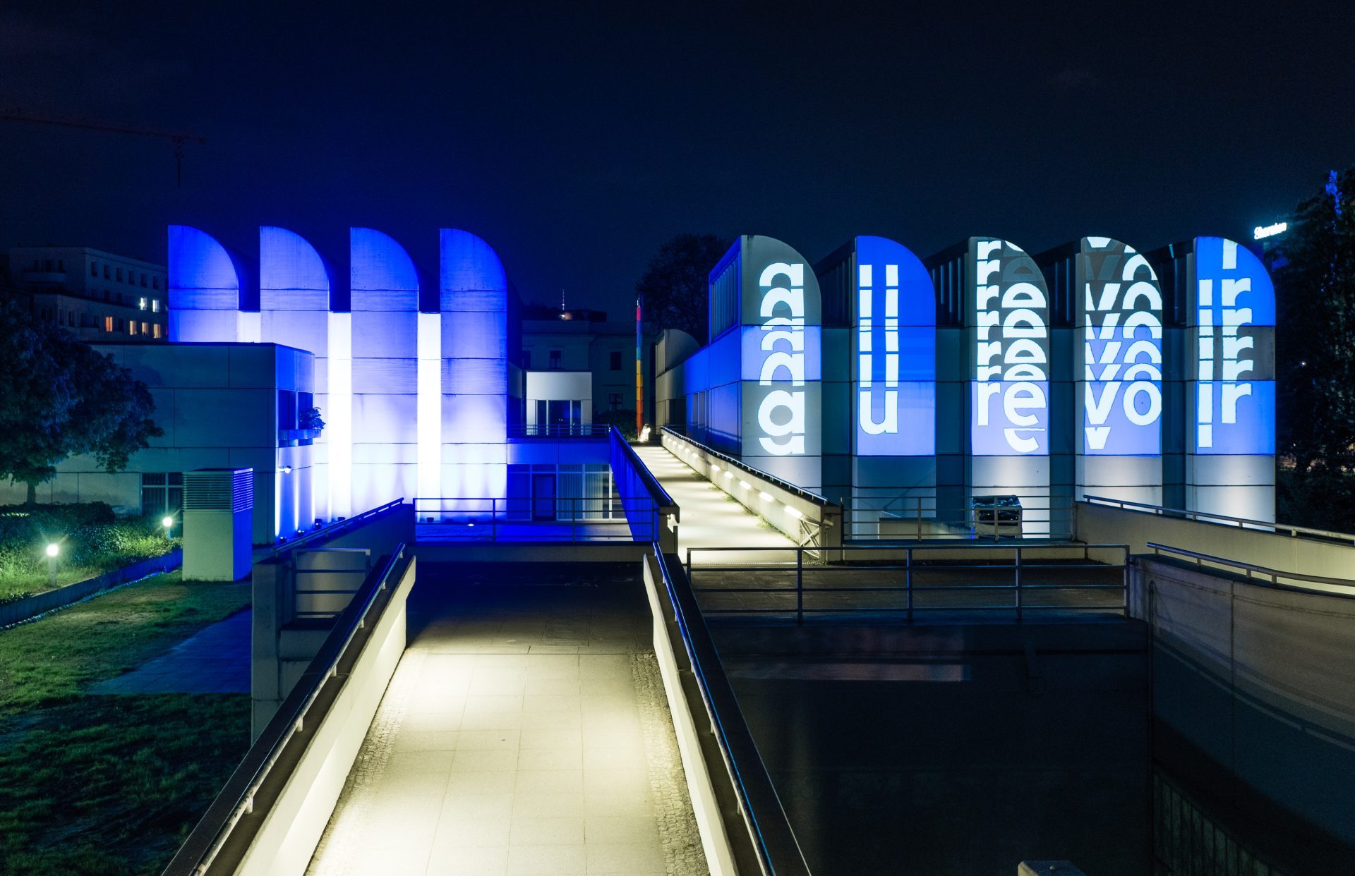 Modernes Gebäude bei Nacht, erleuchtet mit blauen Lichtern und Projektionen auf den Wänden.