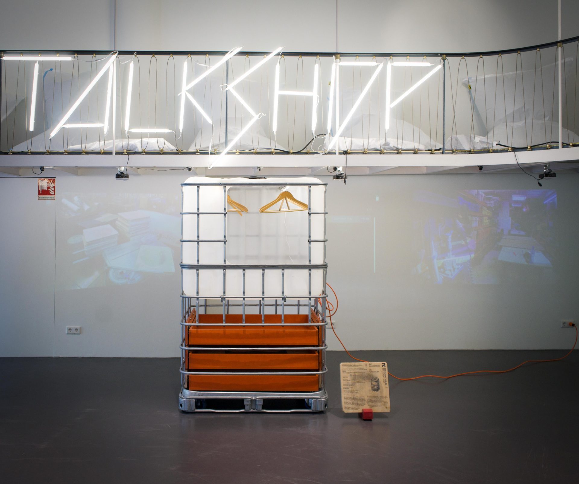 Installation mit skulpturalem Objekt und neonfarbigem Schriftzug "TALK SHOP" im Hintergrund.