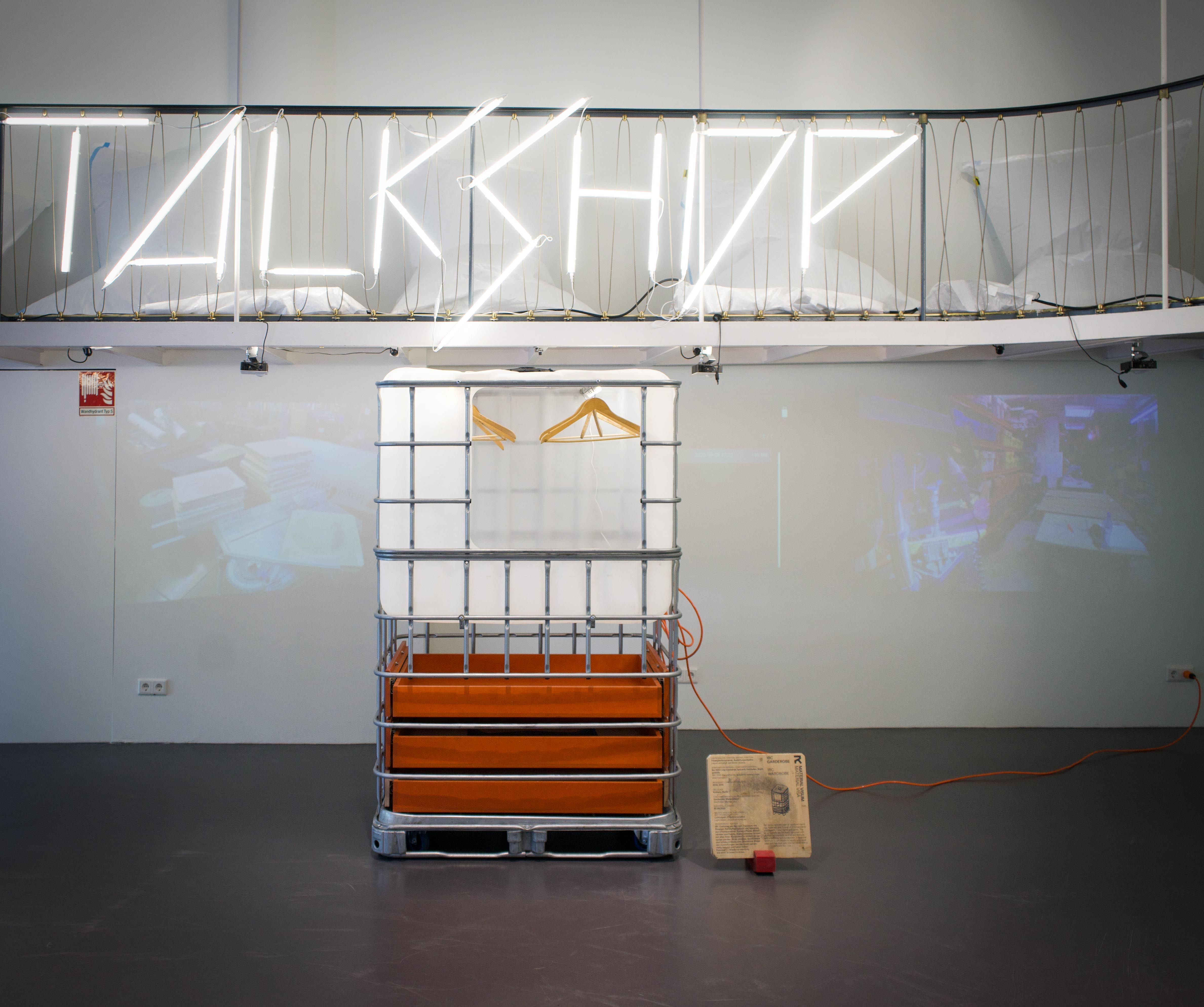 Installation mit skulpturalem Objekt und neonfarbigem Schriftzug "TALK SHOP" im Hintergrund.