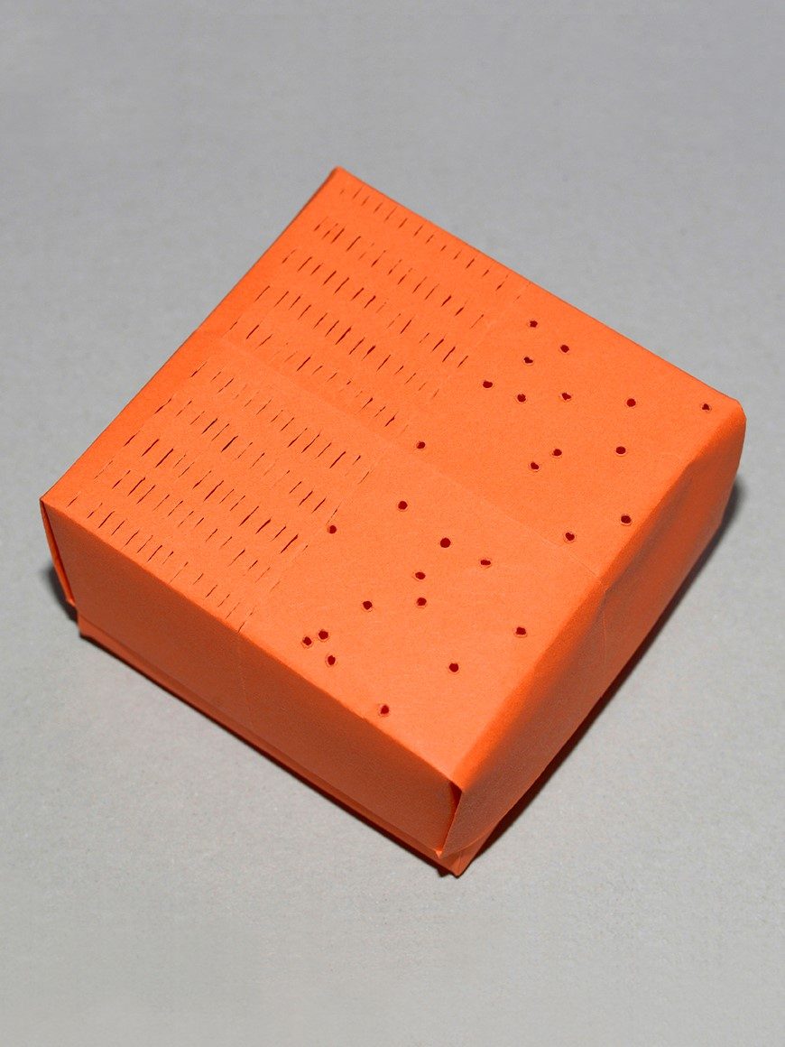 Orangefarbenes Würfel mit durchgehenden Linien und kleinen Löchern auf der Oberfläche.