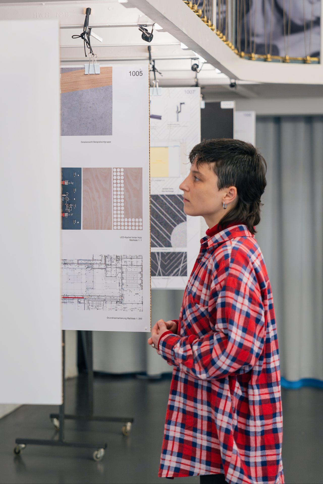 Eine Person mit Kurzhaarschnitt in einem karierten Hemd schaut sich Ausstellungstafeln in einem modernen Raum an.