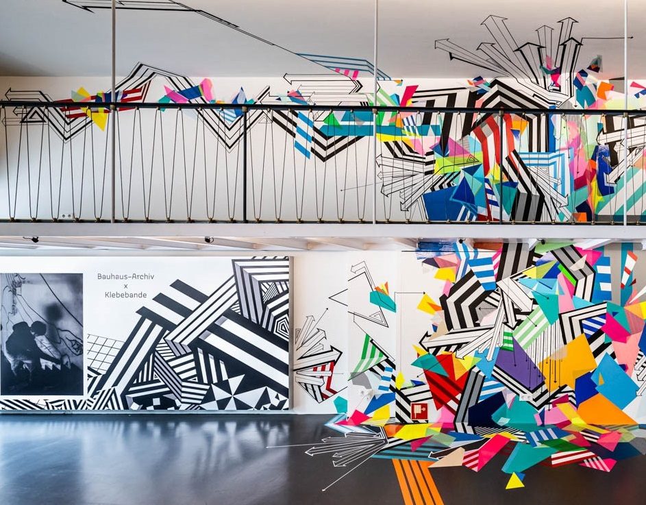 Kunstinstallation mit bunten geometrischen Formen und Linien an Wänden eines modernen Innenraums.