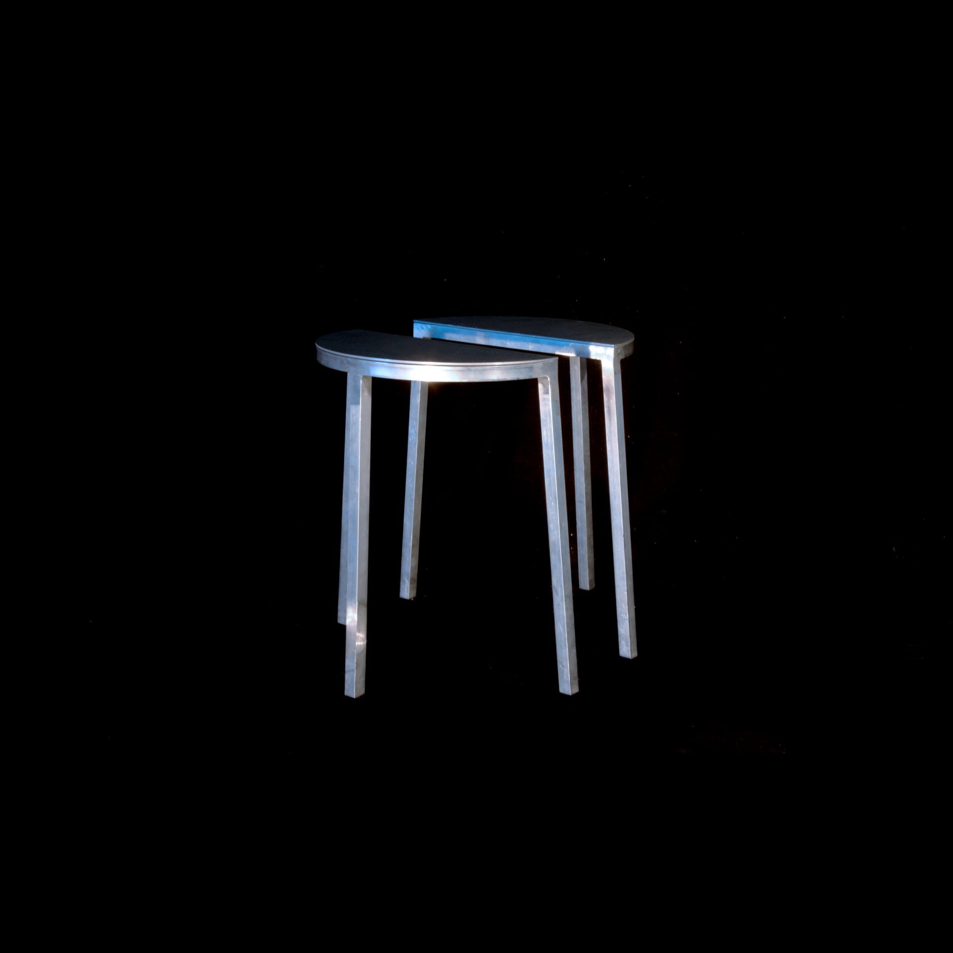 Zwei moderne, schlichte Hocker mit runden Oberflächen vor schwarzem Hintergrund.