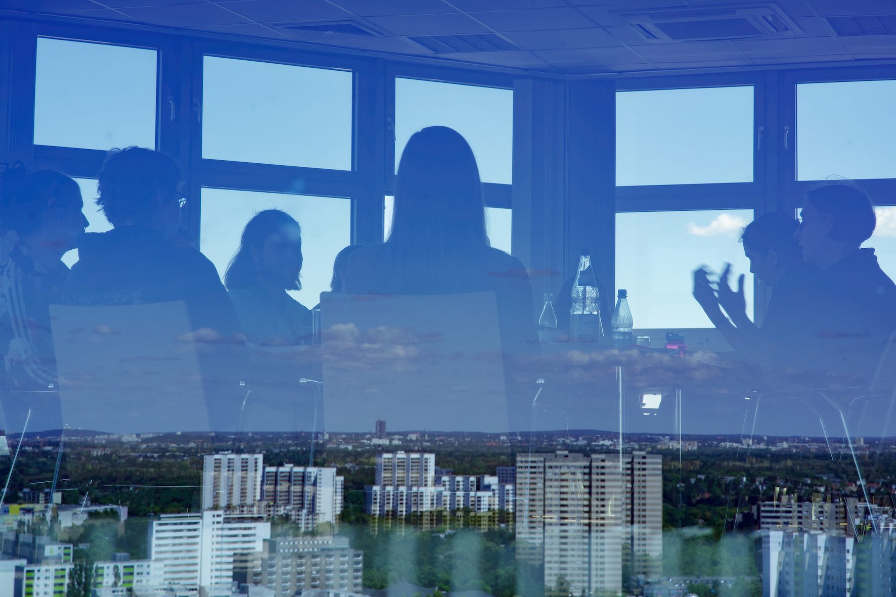 Reflection of people in a conference room with a cityscape in the background.