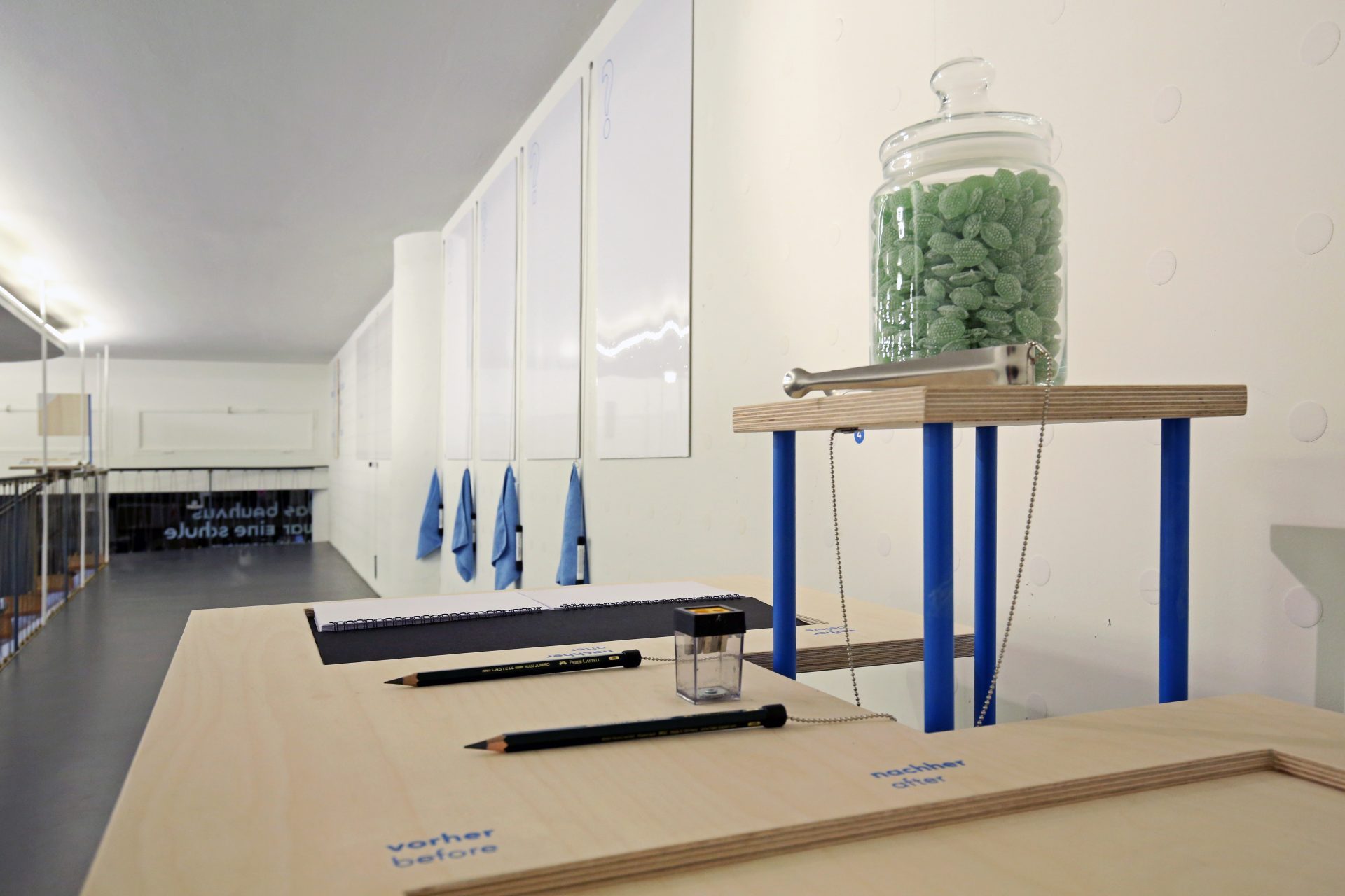 Minimalistische Innenansicht mit Tischen, Stiften und einem Glas gefüllt mit grünen Süßigkeiten.