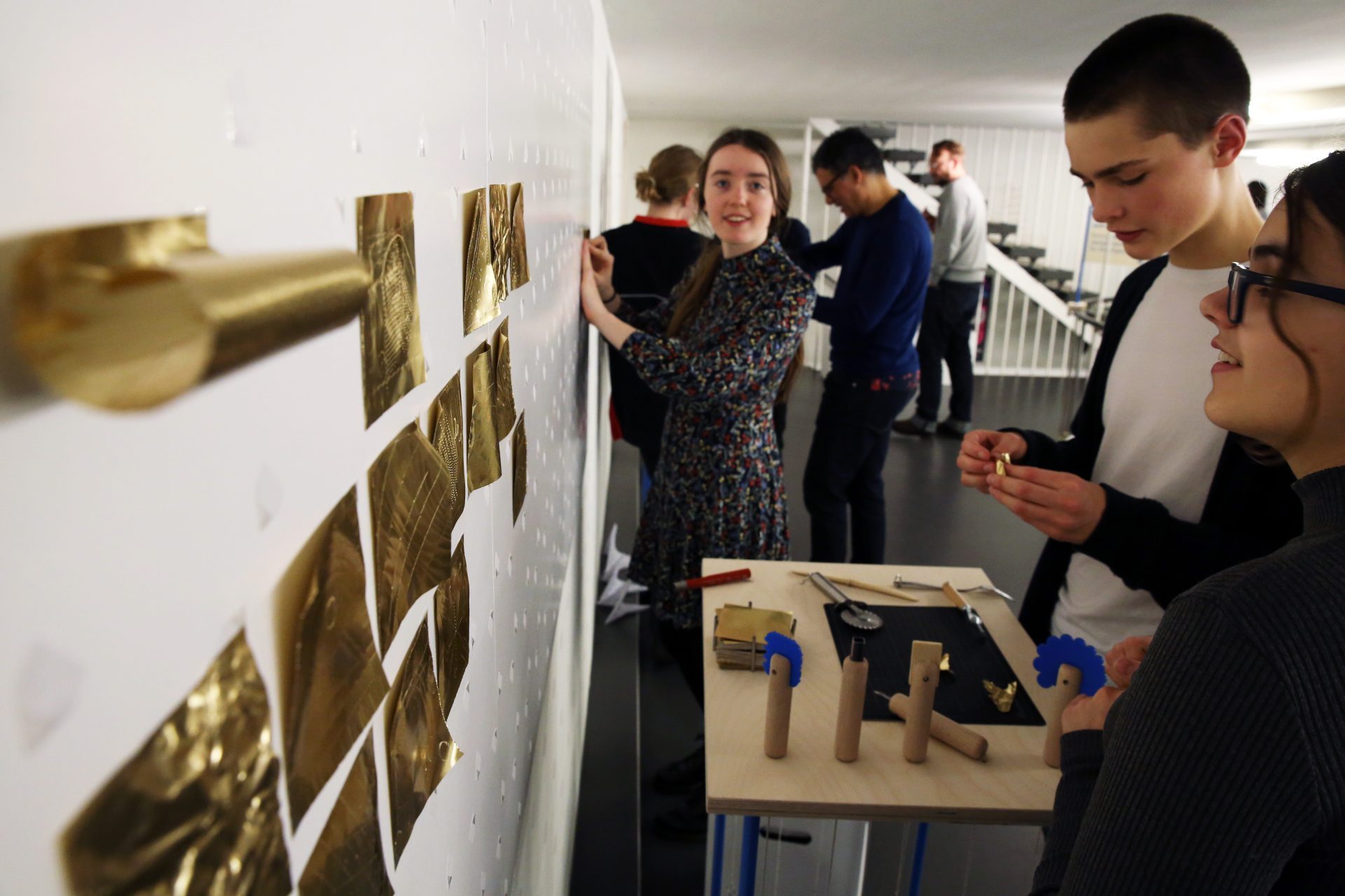 Studenten gestalten an einer Wand ein kreatives Projekt mit verschiedenen Materialien und Formen.