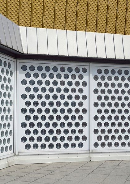 Moderne Wand mit runden Fenstern und schrägem Metallplattendach. Geometrisches Design und helle Farben.