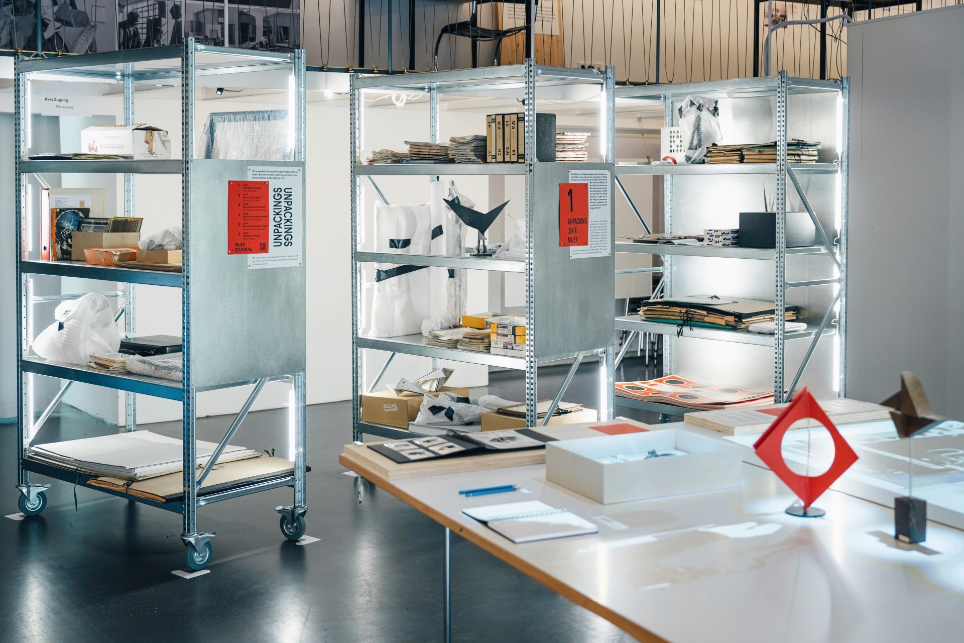 Moderne Ausstellungsräume mit Regalen, die verschiedene Objekte und Materialien bei warmem Licht zeigen.