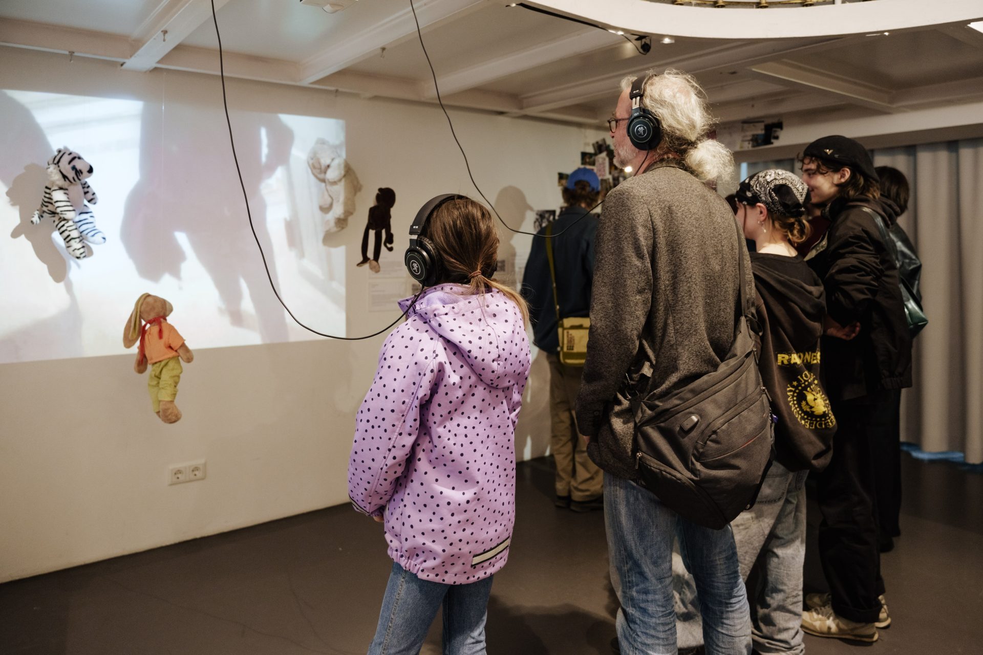 Besuchende in einem Ausstellungsraum betrachten projizierte Bilder und tragen Kopfhörer.