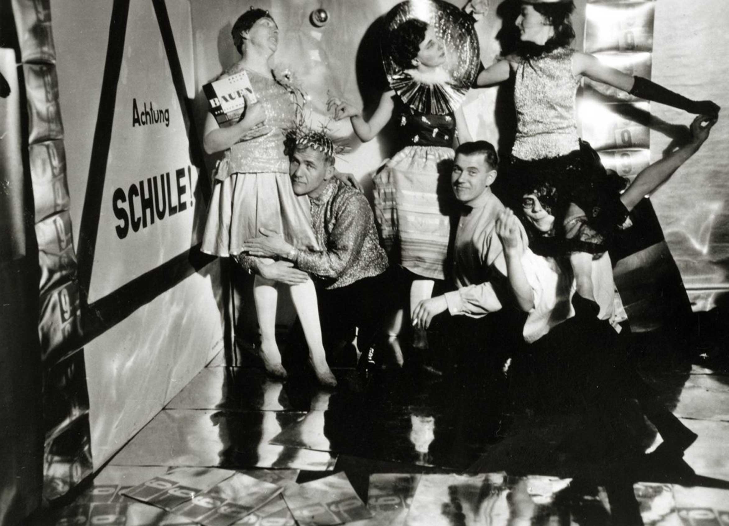A group of people in festive clothing posed in front of a wall with the inscription "Attention School!".