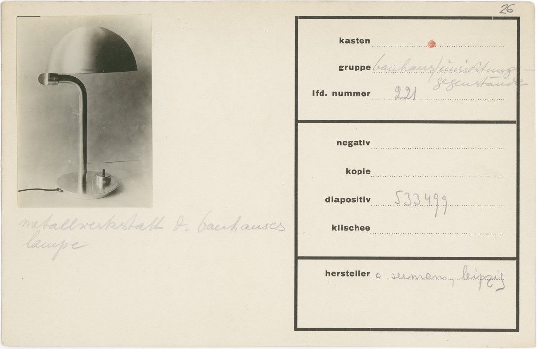 Bauhaus lamp with a shiny metal base and a half-spherical shade on a neutral background.