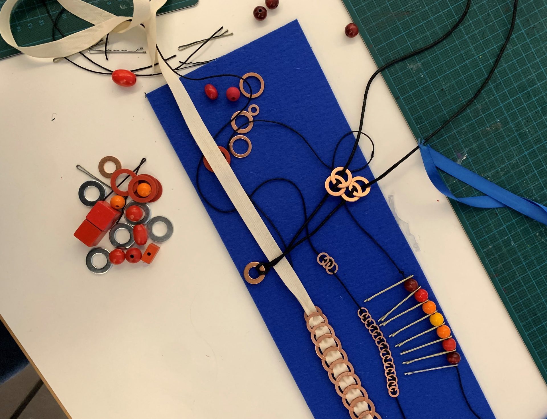 Zu sehen sind für den Workshop verwendetes Material und Schmuckentwürfe auf einem blauen Stoff.
