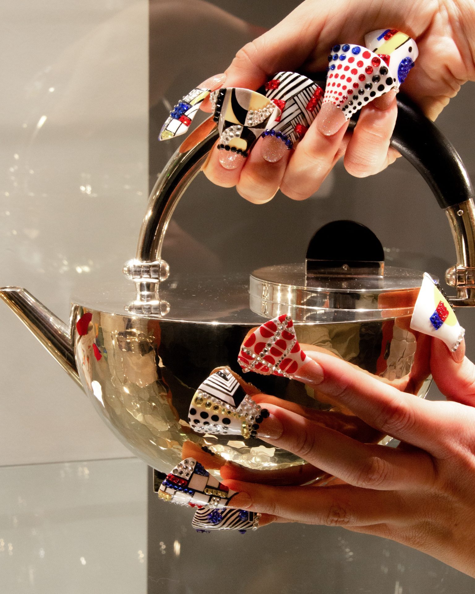 Hände mit bunten, kunstvollen Nägeln halten eine elegante Teekanne.