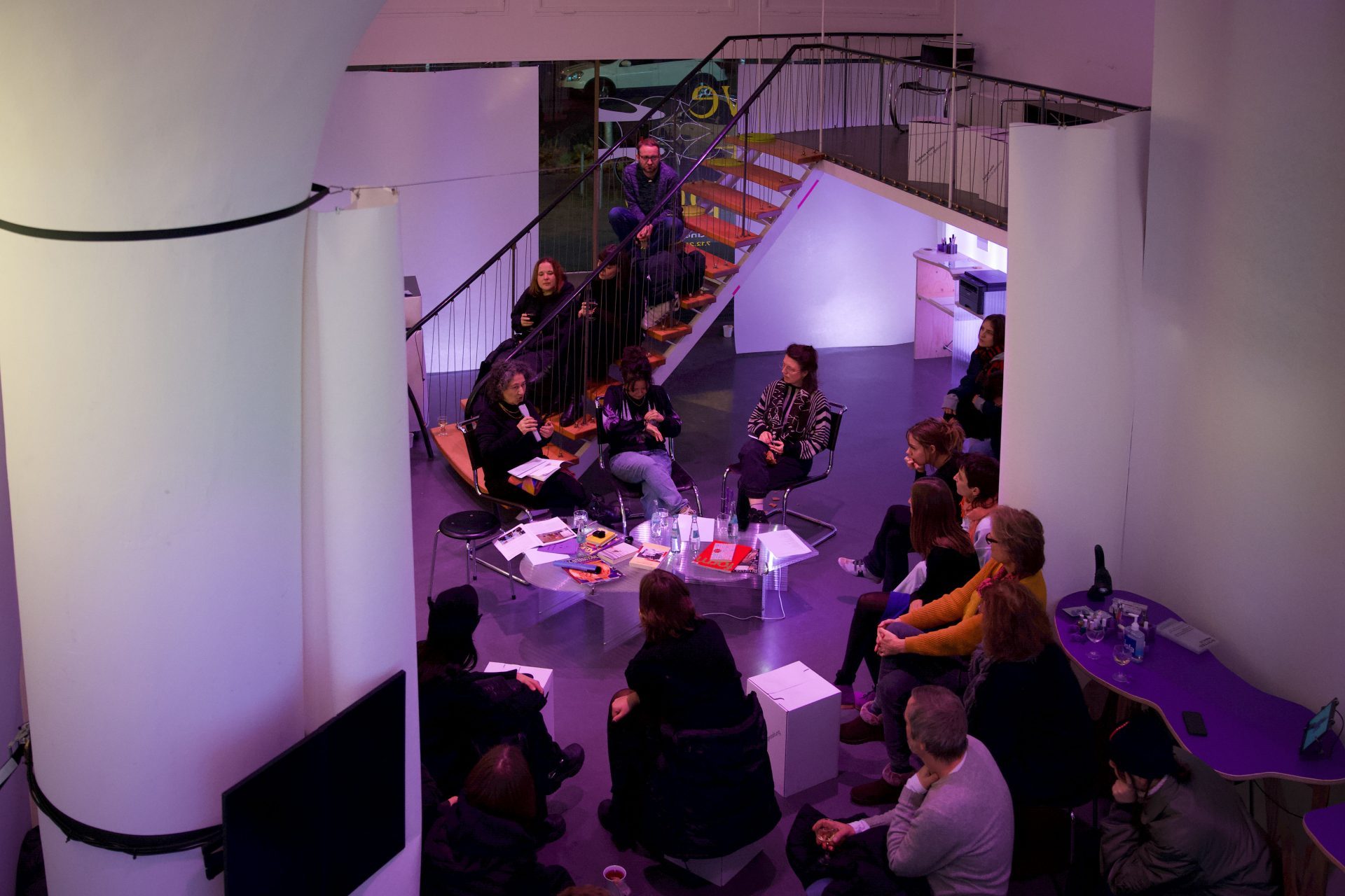 Gruppengespräch in modernem Raum mit viel Licht und bunten Akzenten, Teilnehmer sitzen um einen Tisch.