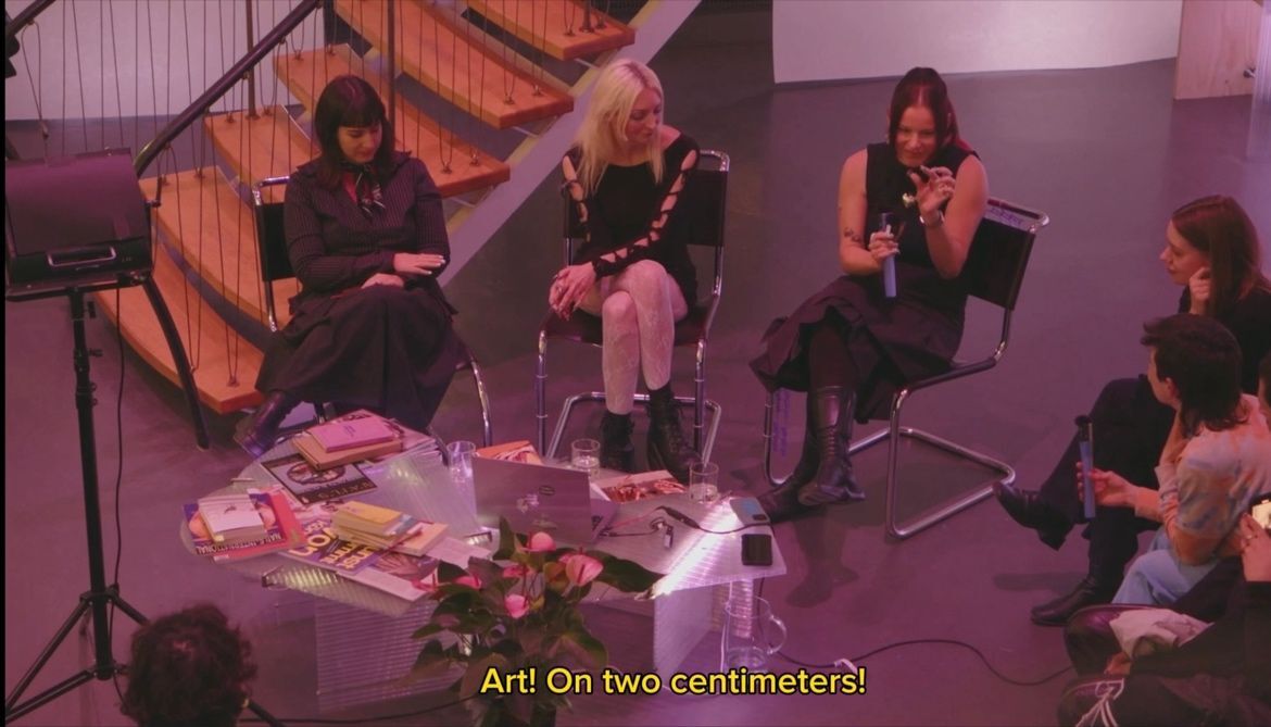 Diskussion über Kunst in modernem Raum mit mehreren Personen auf Stühlen und einem Tisch voller Bücher.
