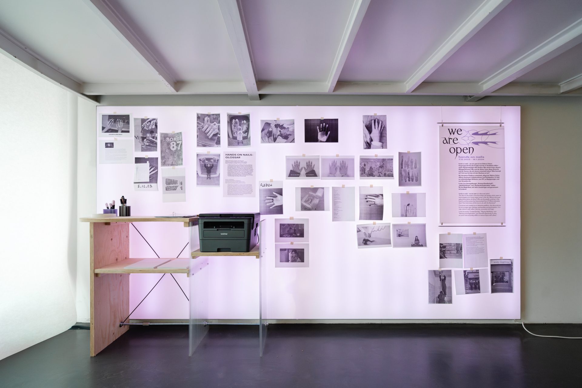 Ein kreativer Raum mit Wandcollage, Drucker und Schreibtisch, umgeben von sanftem Licht.