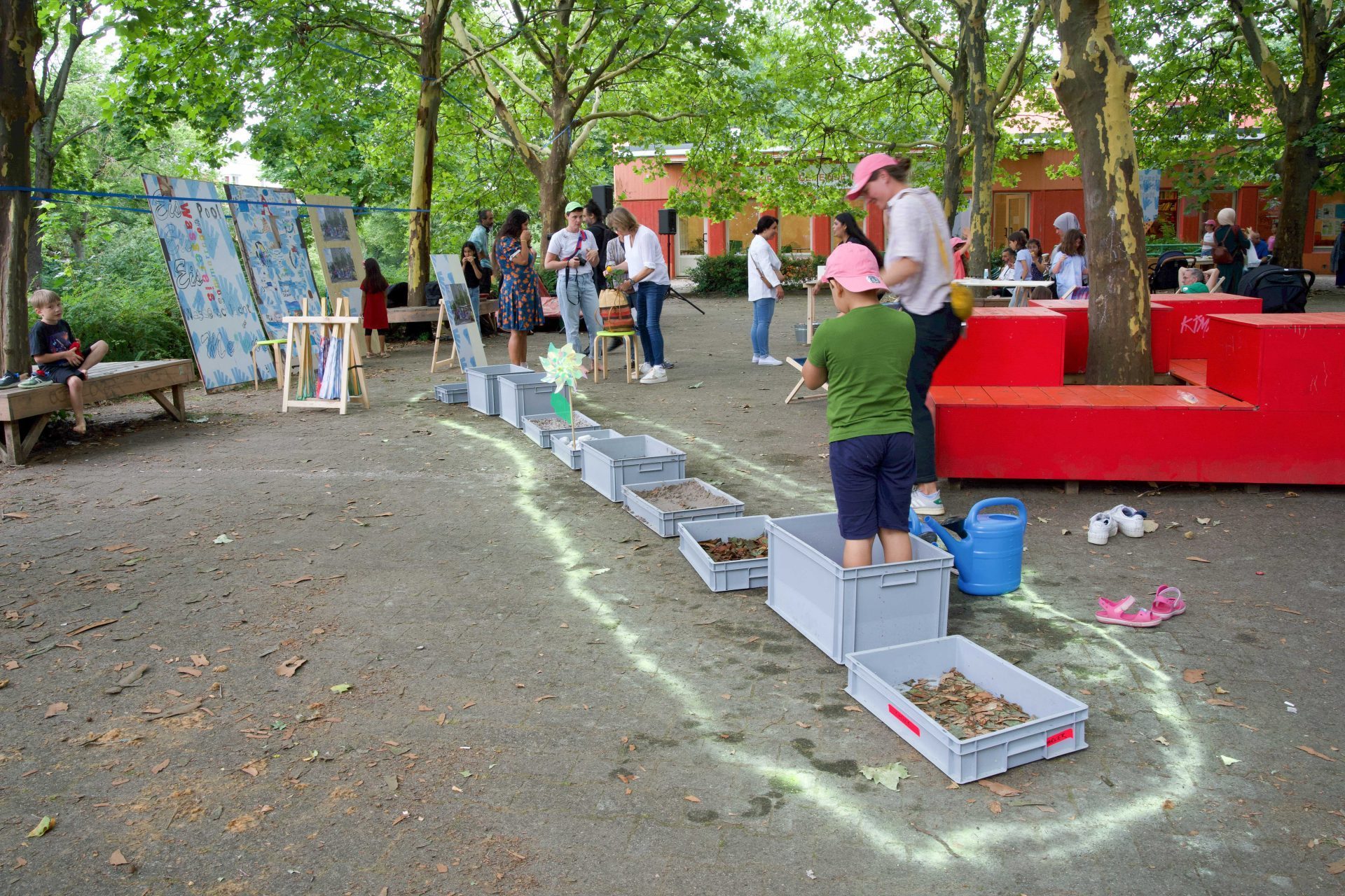Aktivitäten im Freien mit Kindern, Kunstwerken und Materialkisten in einer parkähnlichen Umgebung.