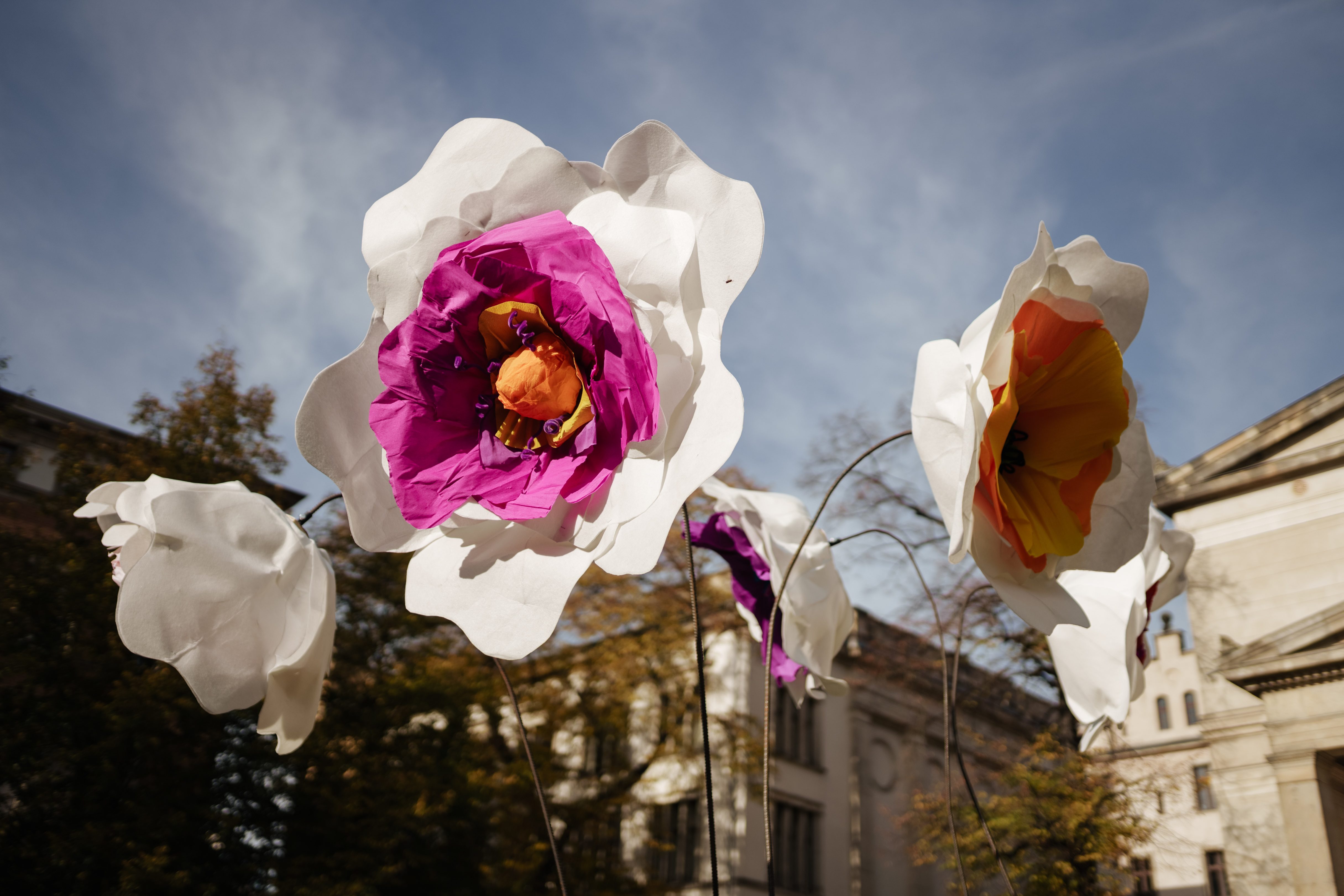 Bunte, große Papierblumen vor historischem Hintergrund und blauem Himmel.