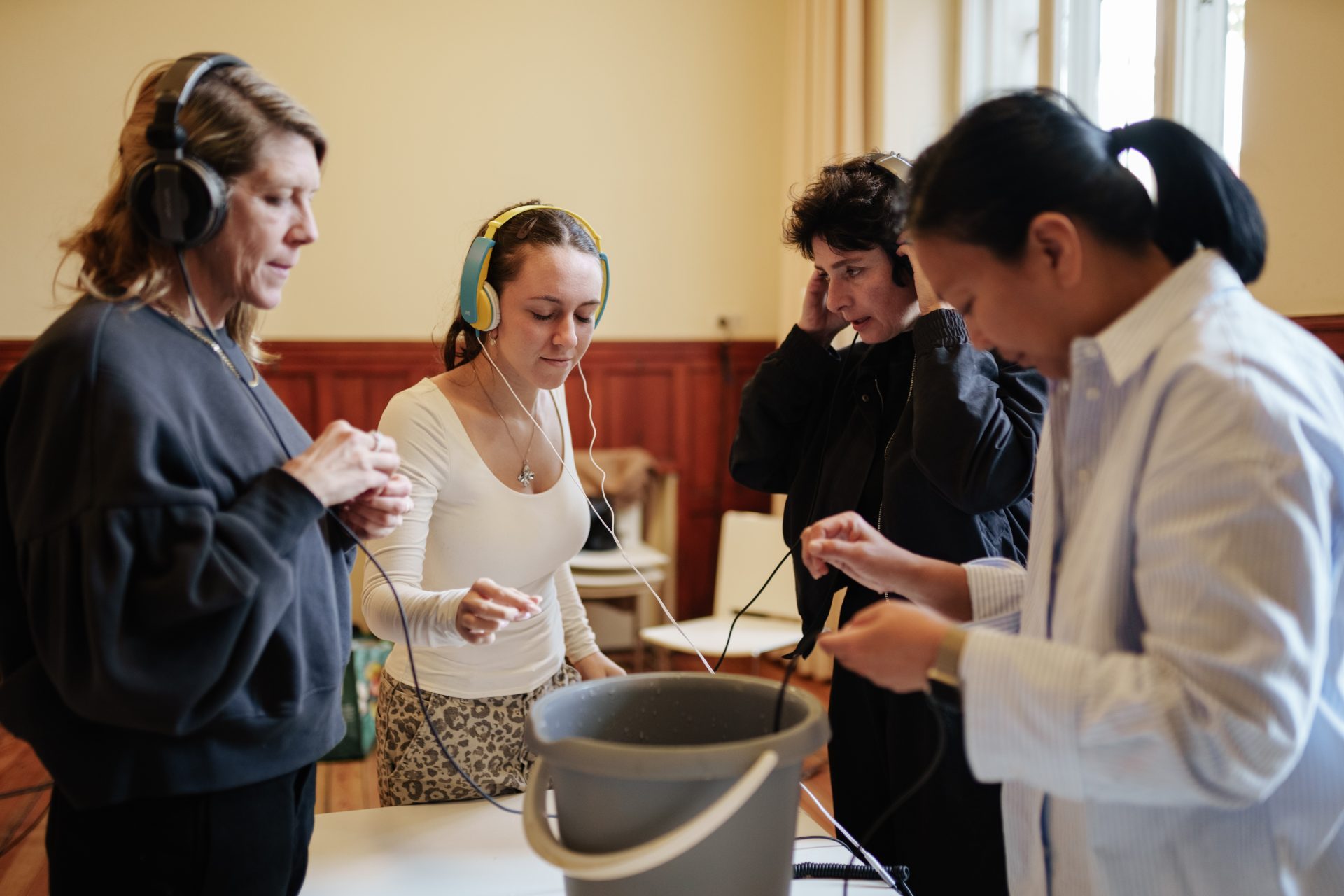 Gruppendiskussion mit vier Personen in Kopfhörern, die an einem Tisch mit einem Eimer experimentieren.