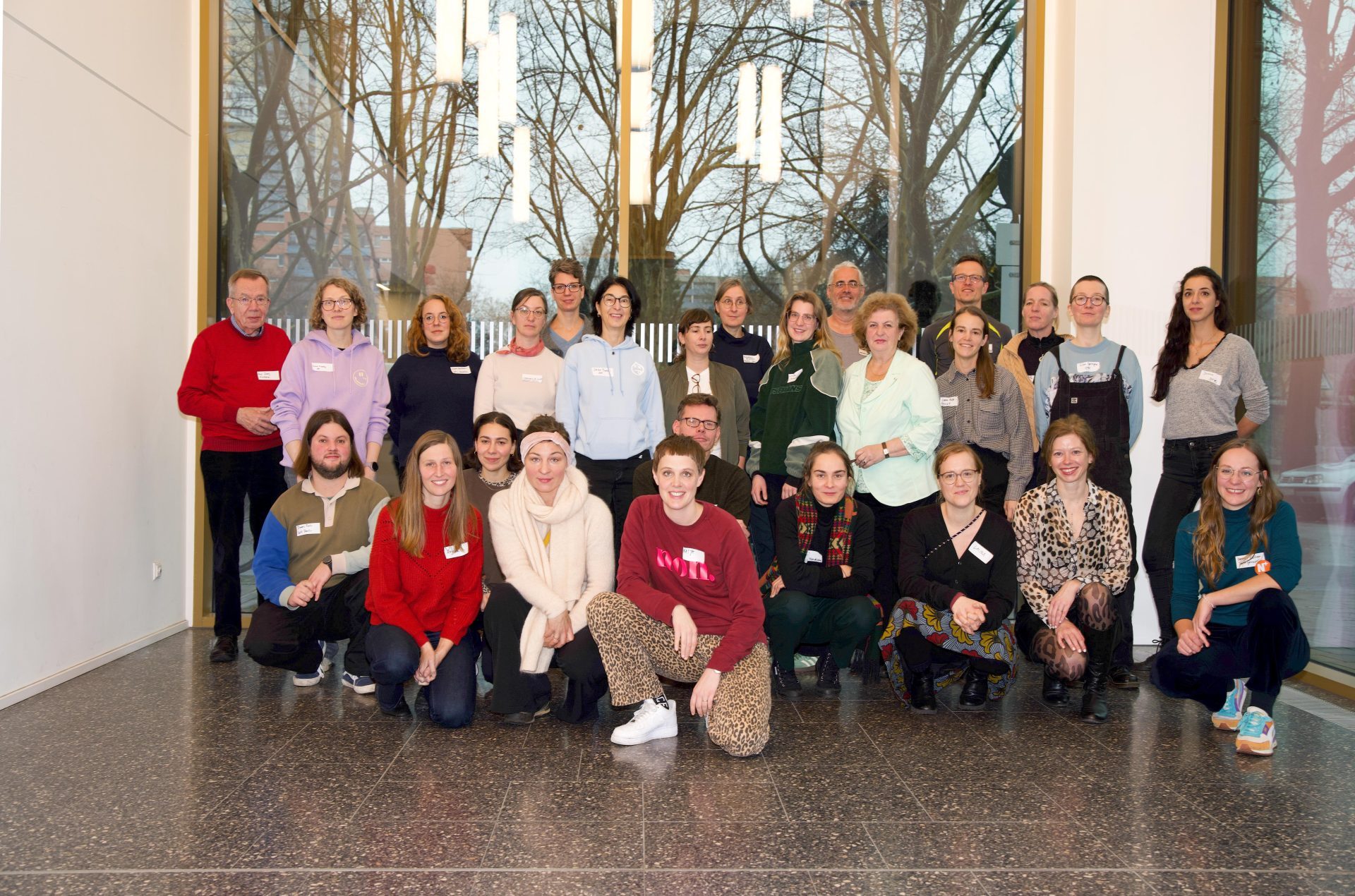 Gruppenfoto von 30 Personen in einem modernen Raum, einige stehen, andere sitzen, alle mit Namensschildern.