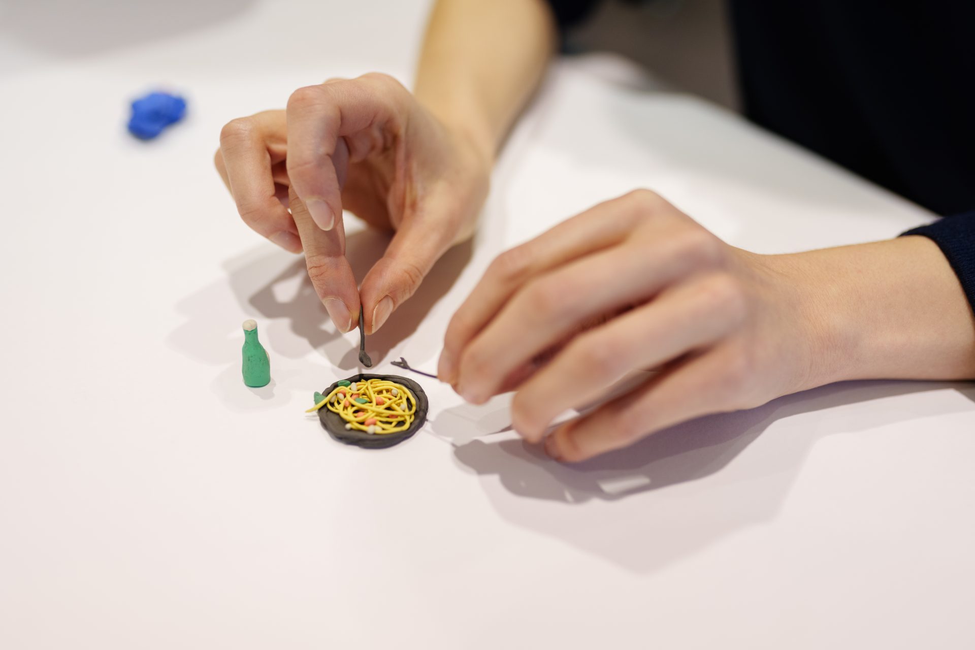 Kreatives Basteln: Jemand formt mit den Händen eine Miniatur aus Knete, die ein Gericht mit Pasta zeigt.