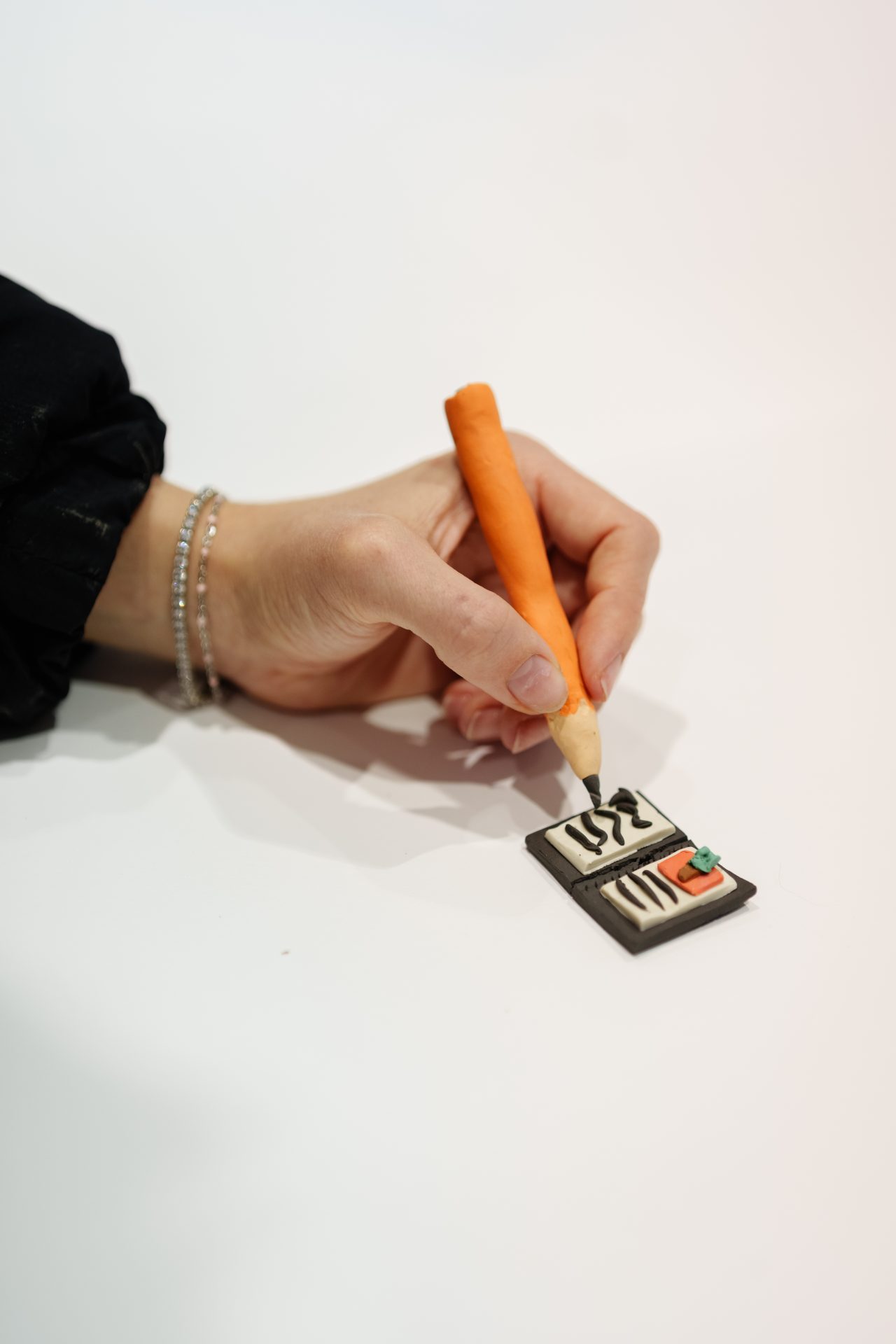 Eine Hand hält einen orangefarbenen Stift und zeichnet auf eine schwarze, kunststoffähnliche Fläche.