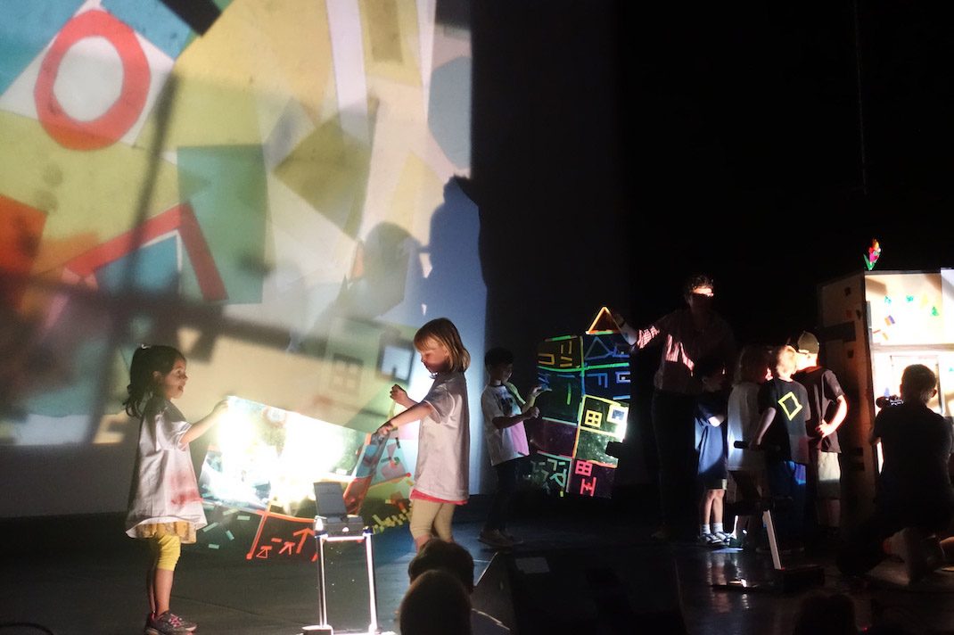 Kinder experimentieren mit Licht und Farben und kreieren kreative Kunstwerke auf einer Bühne.