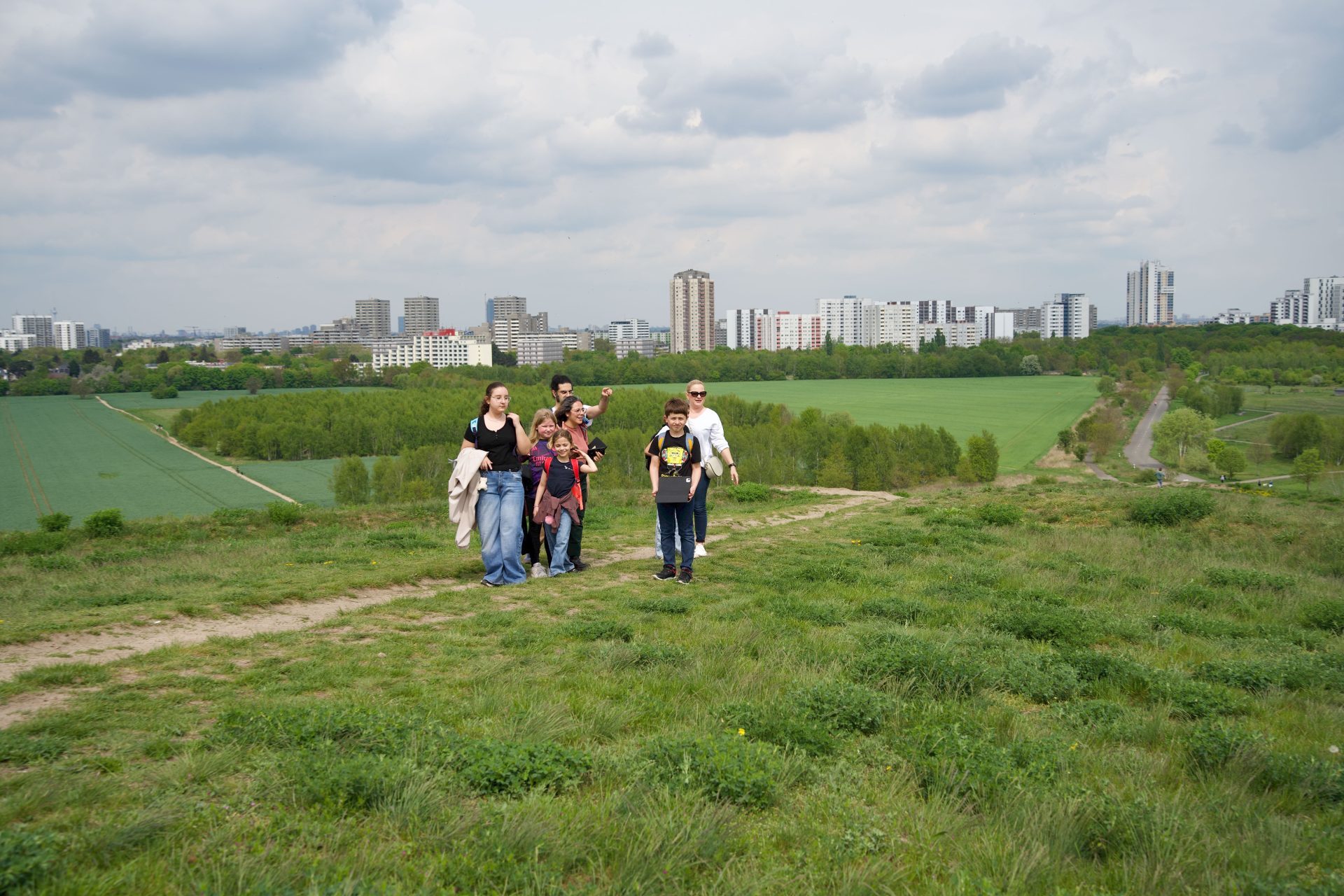 Gruppe von Menschen wandert über einen Hügel mit Blick auf eine Stadt und grüne Felder.