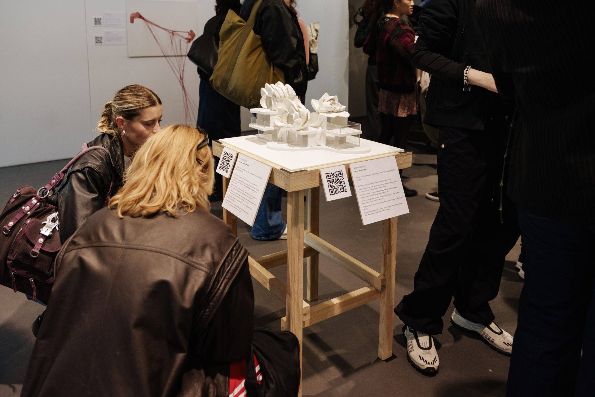 Zwei Personen betrachten eine Skulptur auf einem Tisch, umgeben von anderen Besuchern der Ausstellung.