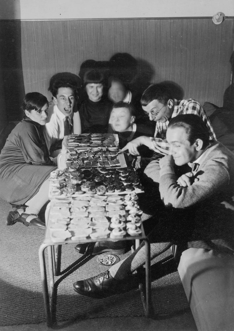Gruppe von Menschen sitzt an einem Tisch mit Leckereien in einem gemütlichen Raum. Schwarz-Weiß-Foto.
