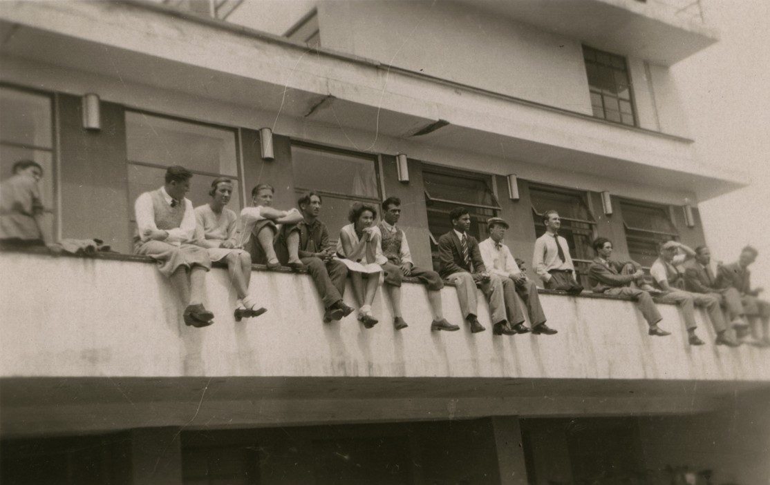 Gruppe von Personen, die auf einer Gebäudekante sitzen. Schwarz-weiß-Foto.