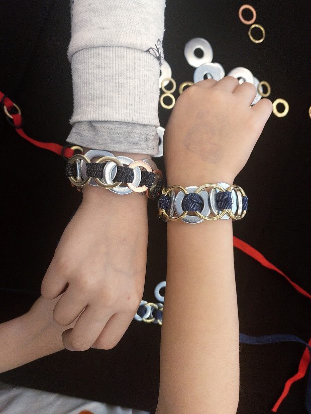Das Bild zeigt zwei Kinderarme mit Armbändern aus Metallringen.