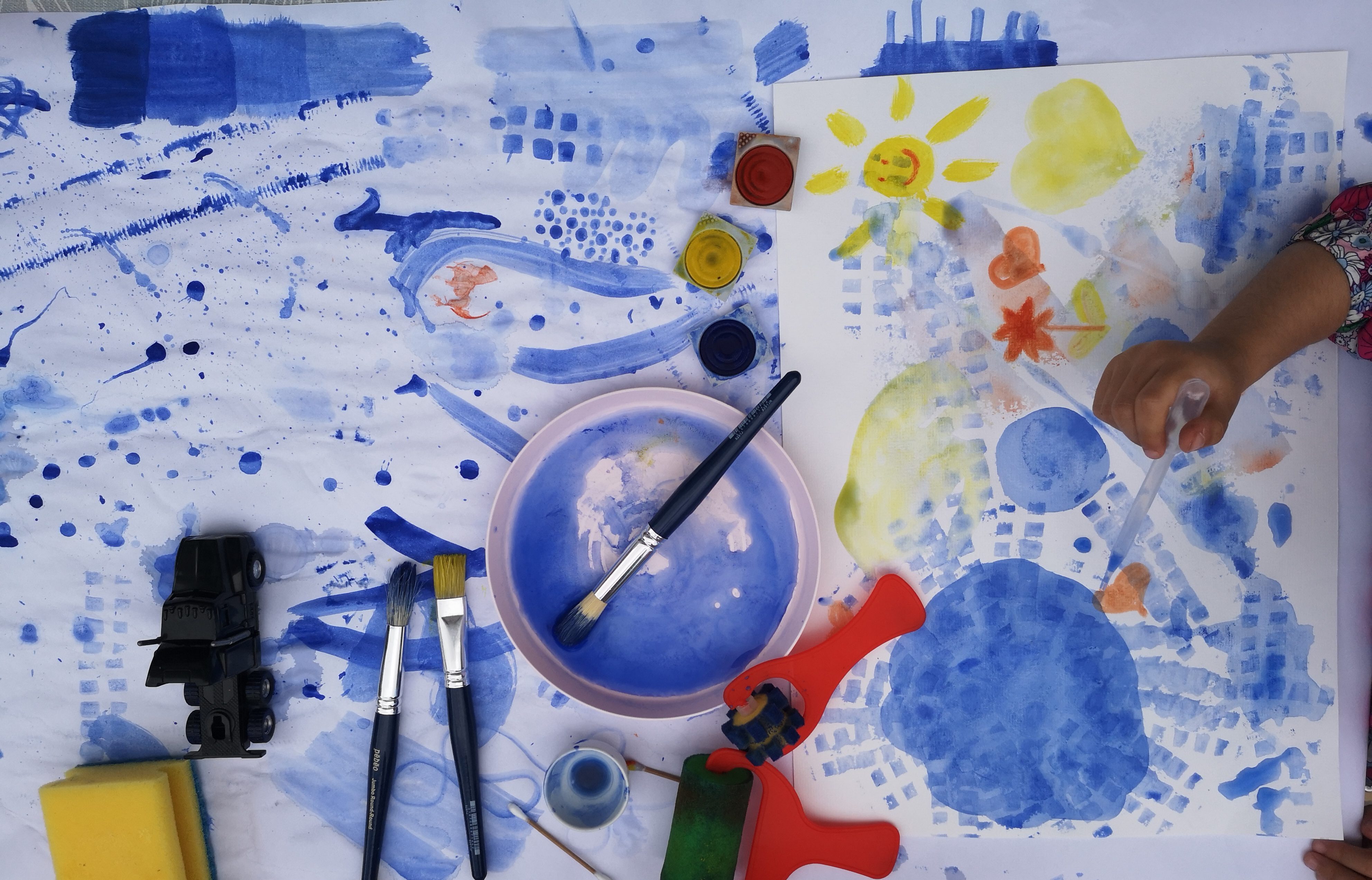 Buntes Kunstwerk mit blauen Farbtönen, Pinseln und kreativen Materialien auf einem Tisch.