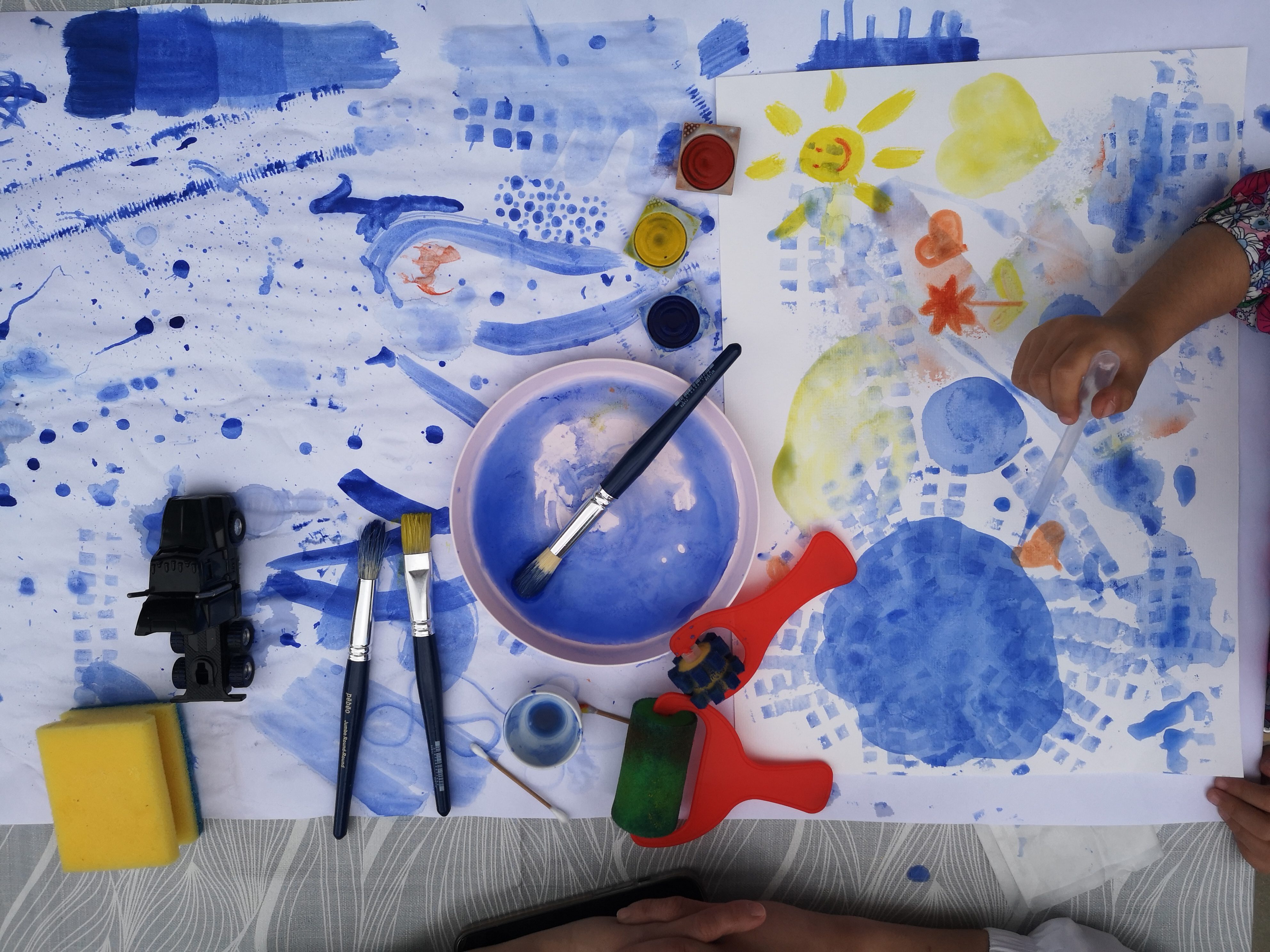 Colorful artwork featuring blue tones, brushes, water, and creative materials on a table.