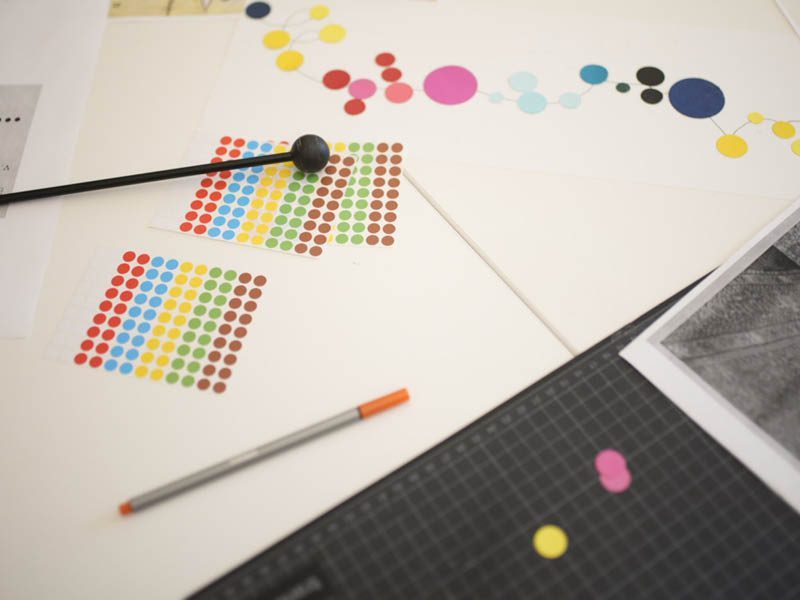 Bunt bedruckte Papiermuster mit Farbkugeln und einem Stift auf einem Tisch, umgeben von verschiedenen Farben.